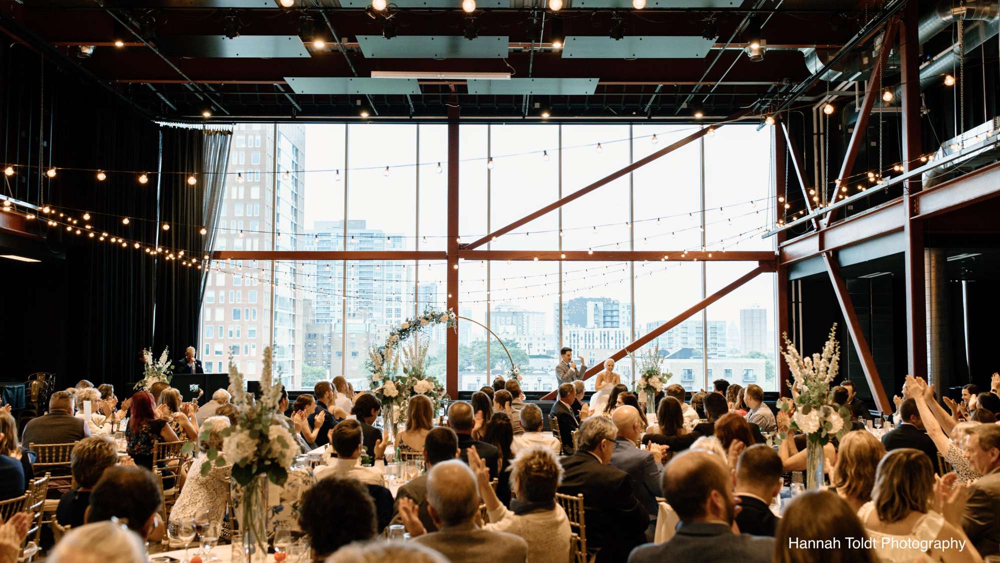 A heartfelt toast by the couple, framed by the city skyline, during their reception at Jan Serr Studio.