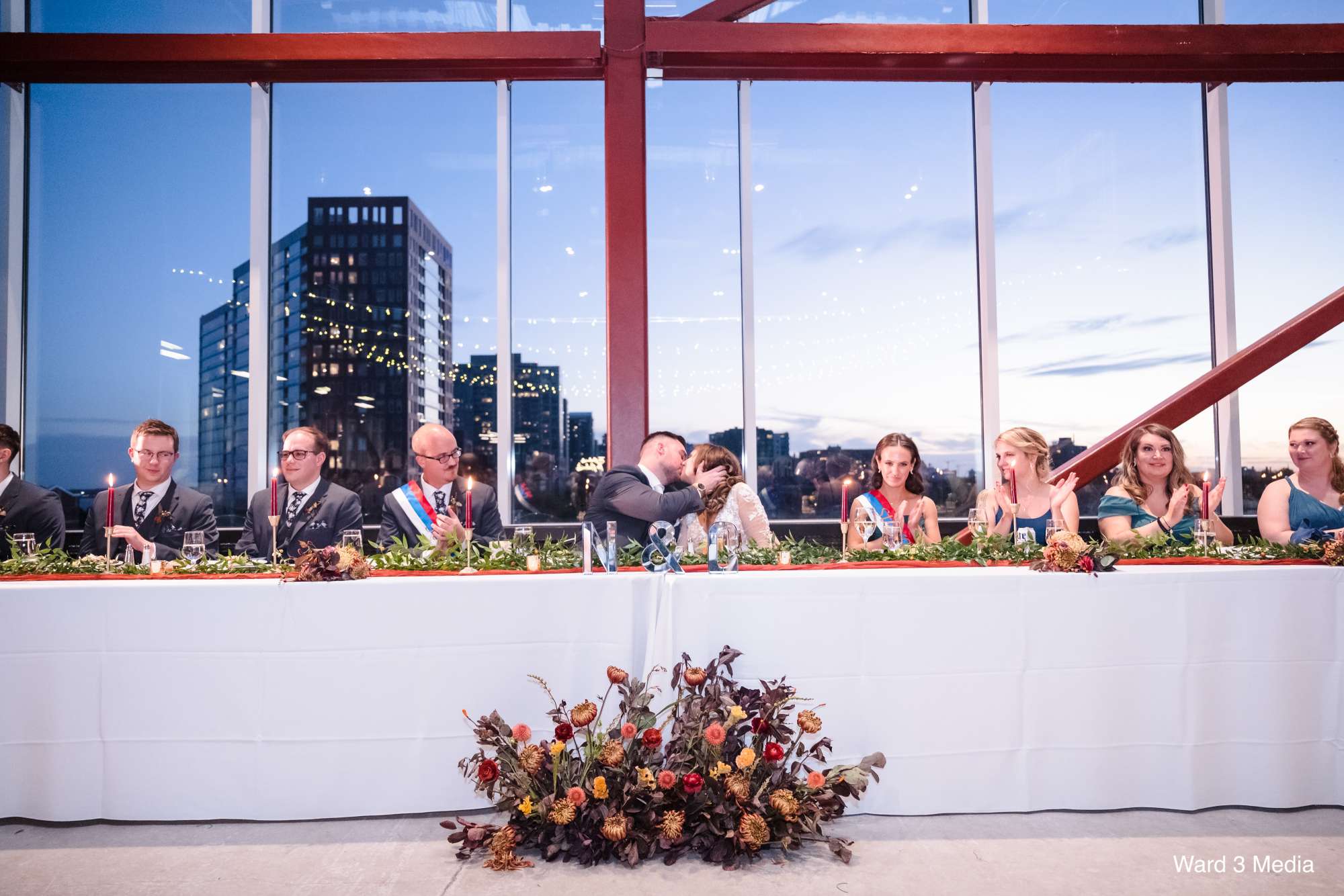 A beautifully decorated head table with flowers and candles, set against the backdrop of the studio's signature floor-to-ceiling windows.