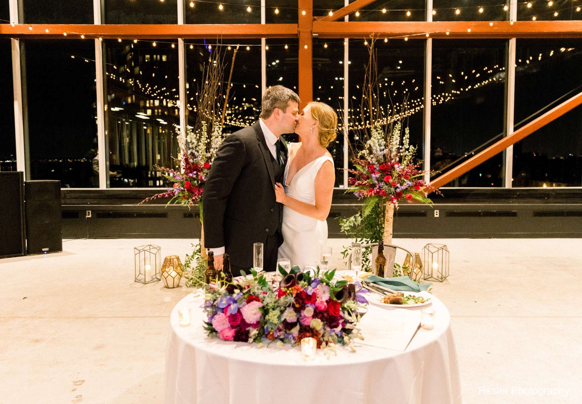 The couple’s intimate sweetheart table adorned with vibrant floral arrangements and candlelight, placed in front of the expansive windows.