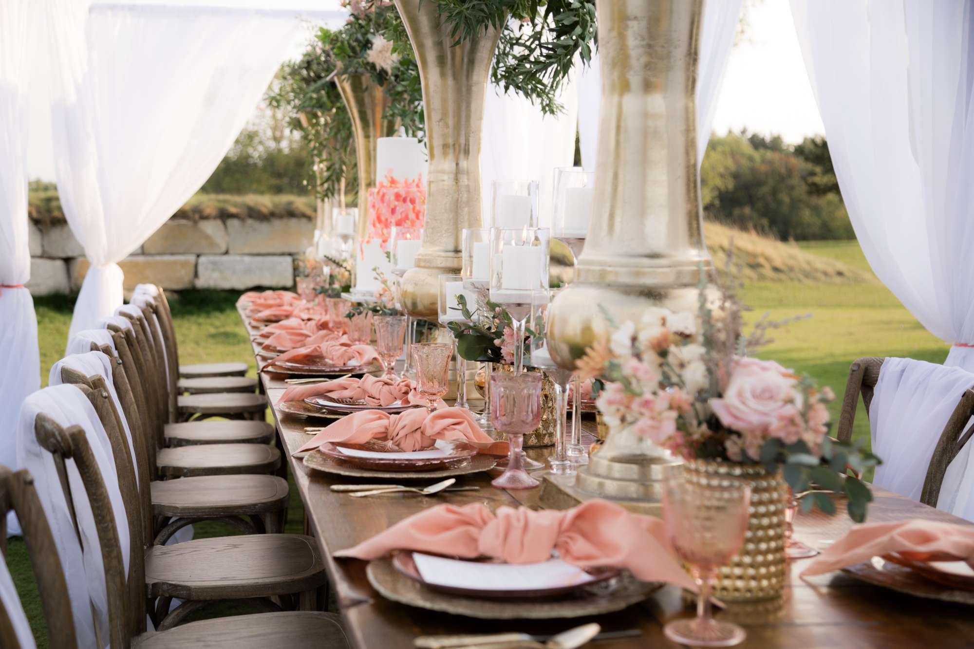 An elegant outdoor tablescape designed by Ambrosia Events, featuring blush details, lush florals, and golden decor.
