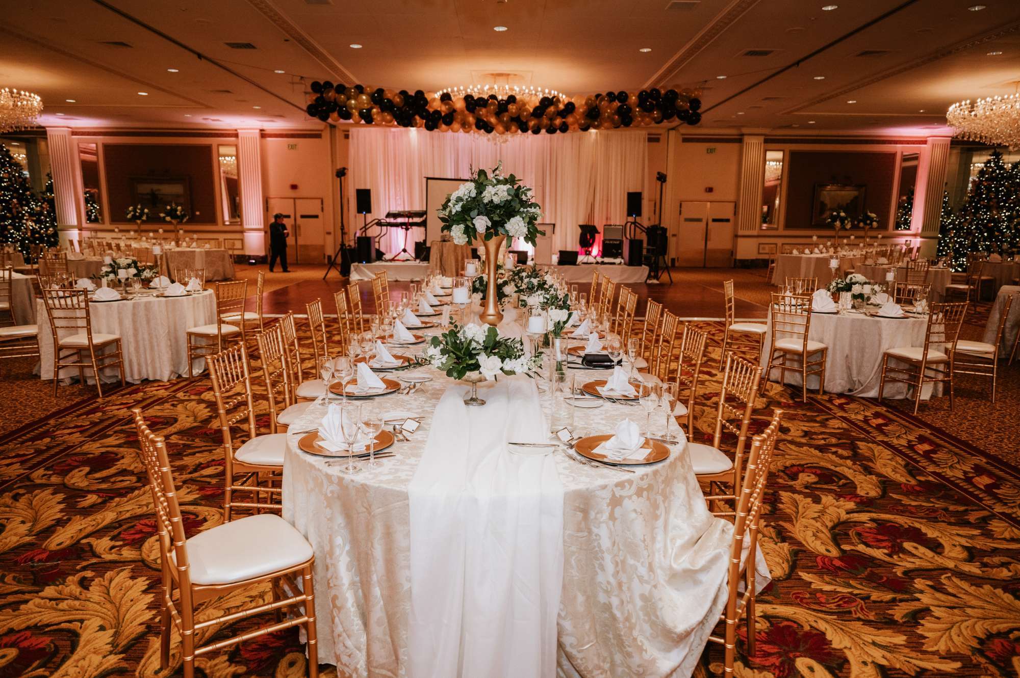 Ambrosia Events transforms this grand reception hall with luxurious gold accents and floral centerpieces for an unforgettable celebration.