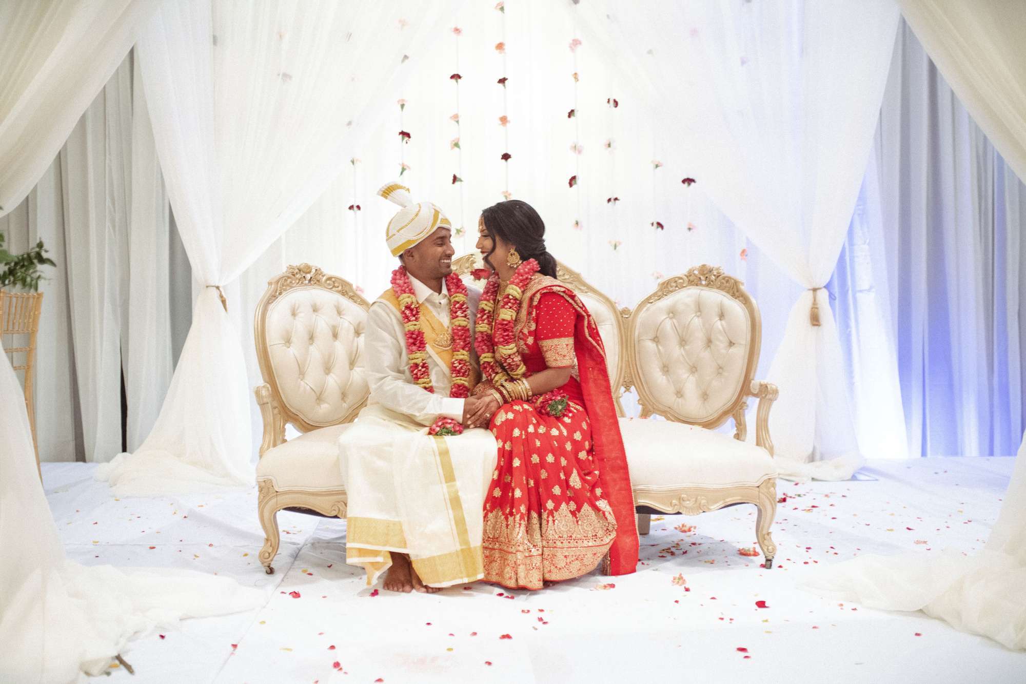 Ambrosia Events designed this elegant Indian wedding stage with soft draping, a luxurious couch, and romantic floral garlands.
