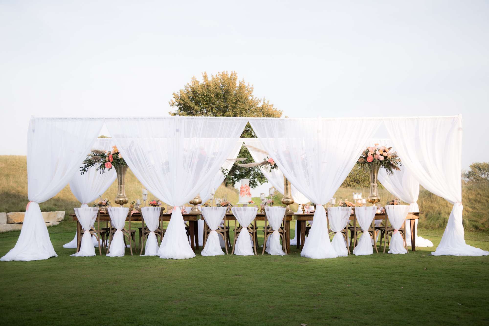 Ambrosia Events created a breathtaking custom outdoor wedding reception featuring airy white drapes and floral centerpieces.