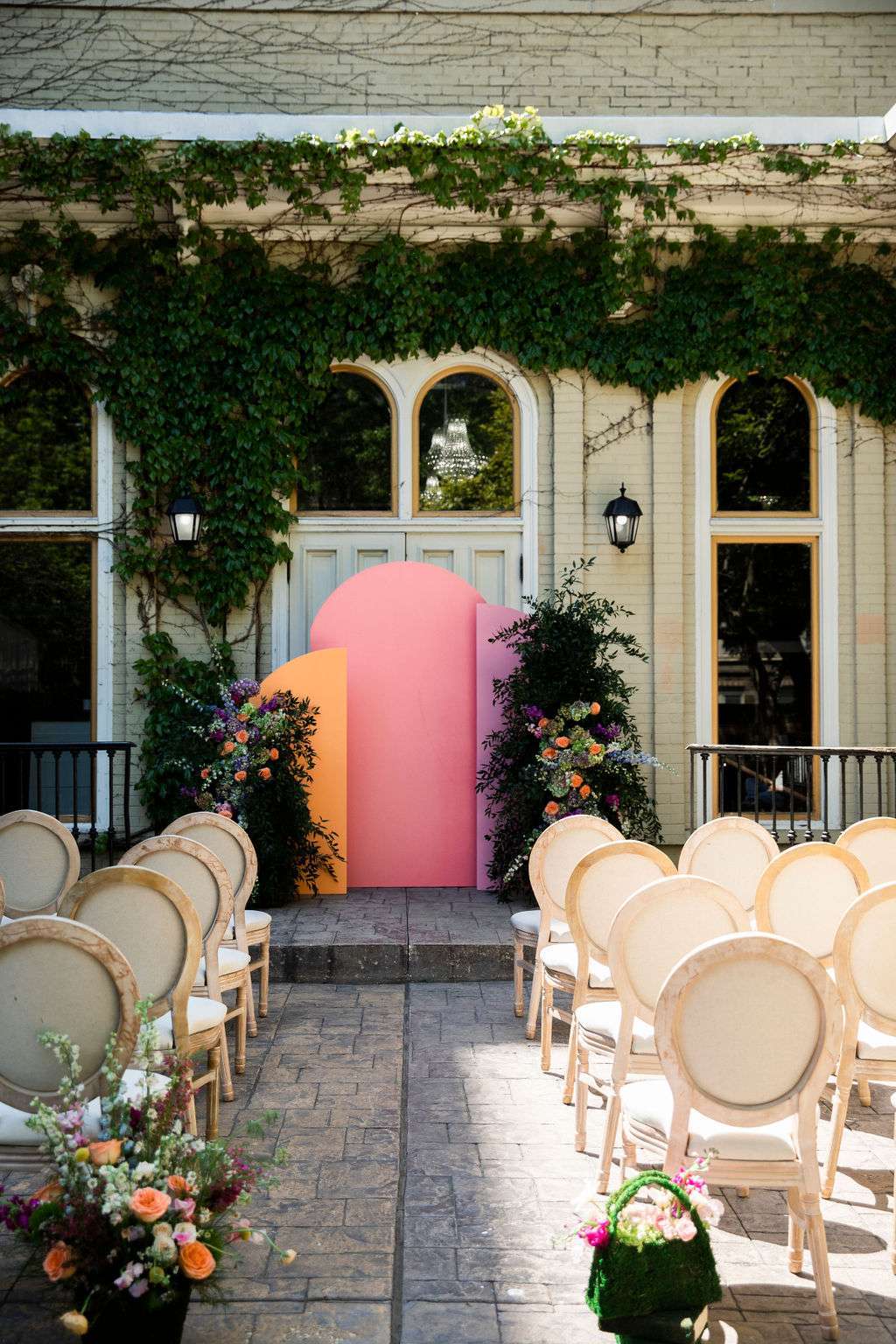A whimsical ceremony backdrop by Ambrosia Events with colorful floral arrangements and modern, vibrant arches.