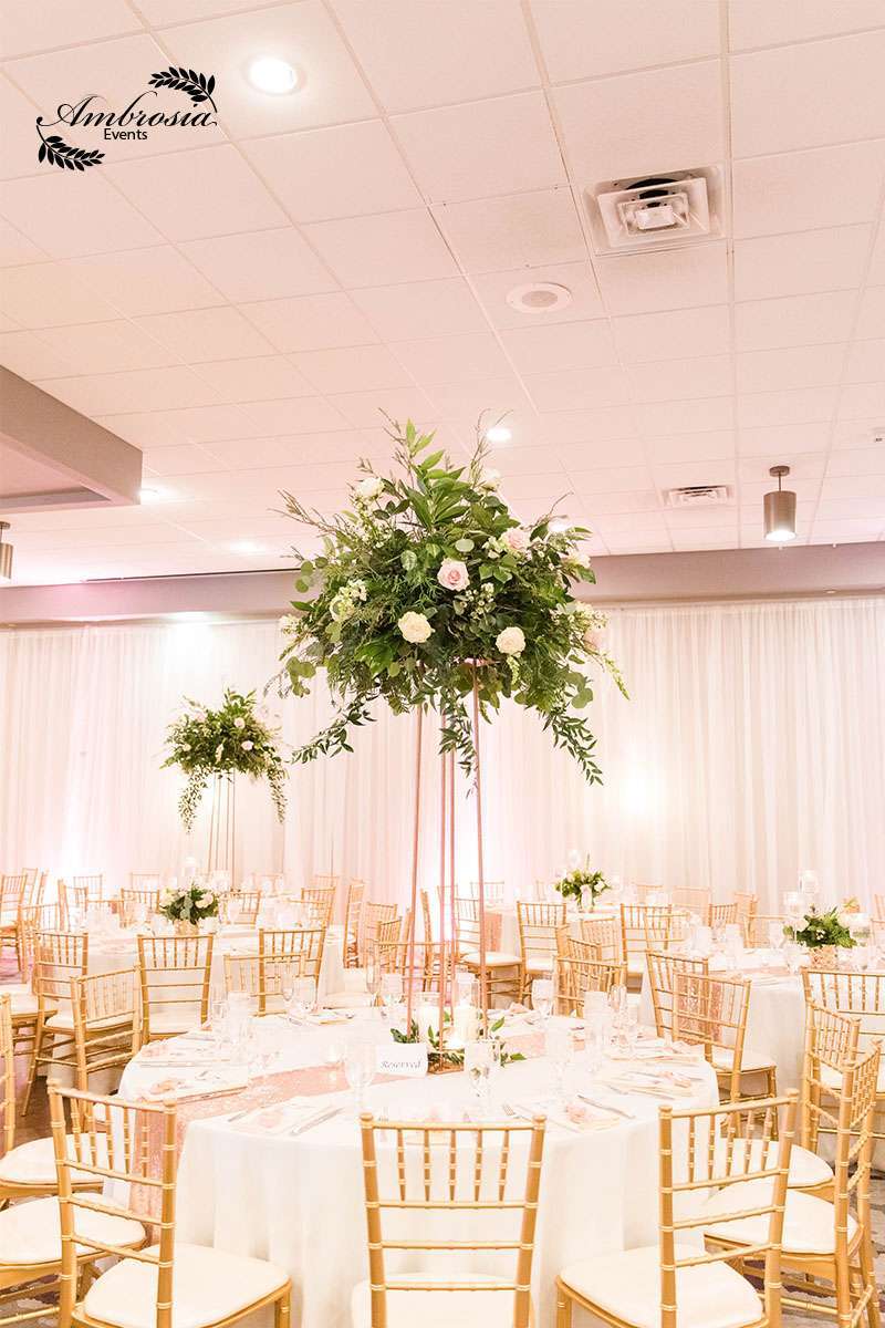 Ambrosia Events designed this luxurious wedding reception with tall greenery centerpieces and soft gold accents.
