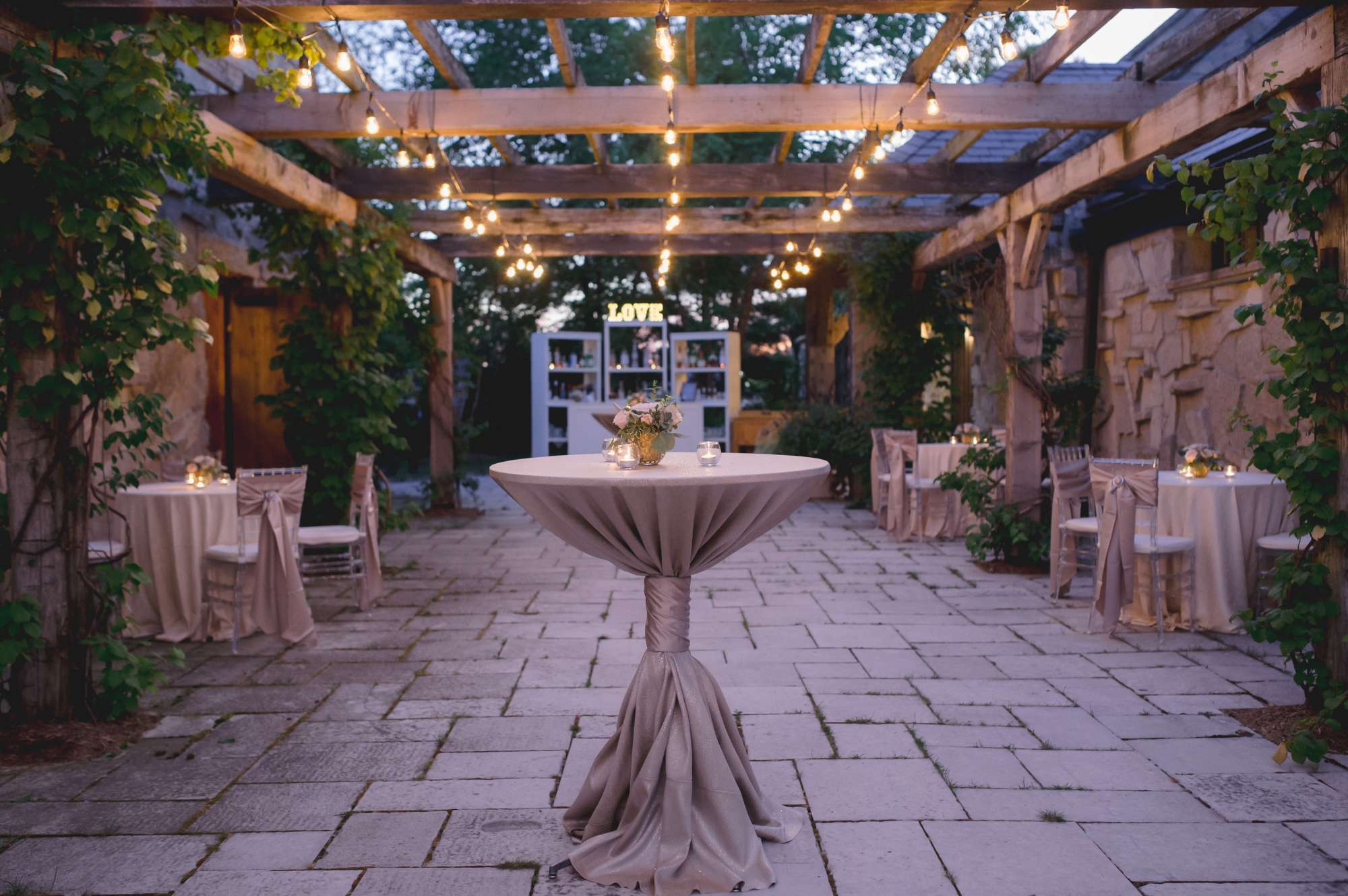 A romantic evening setting styled by Ambrosia Events, featuring intimate lighting, stone architecture, and elegant cocktail tables.