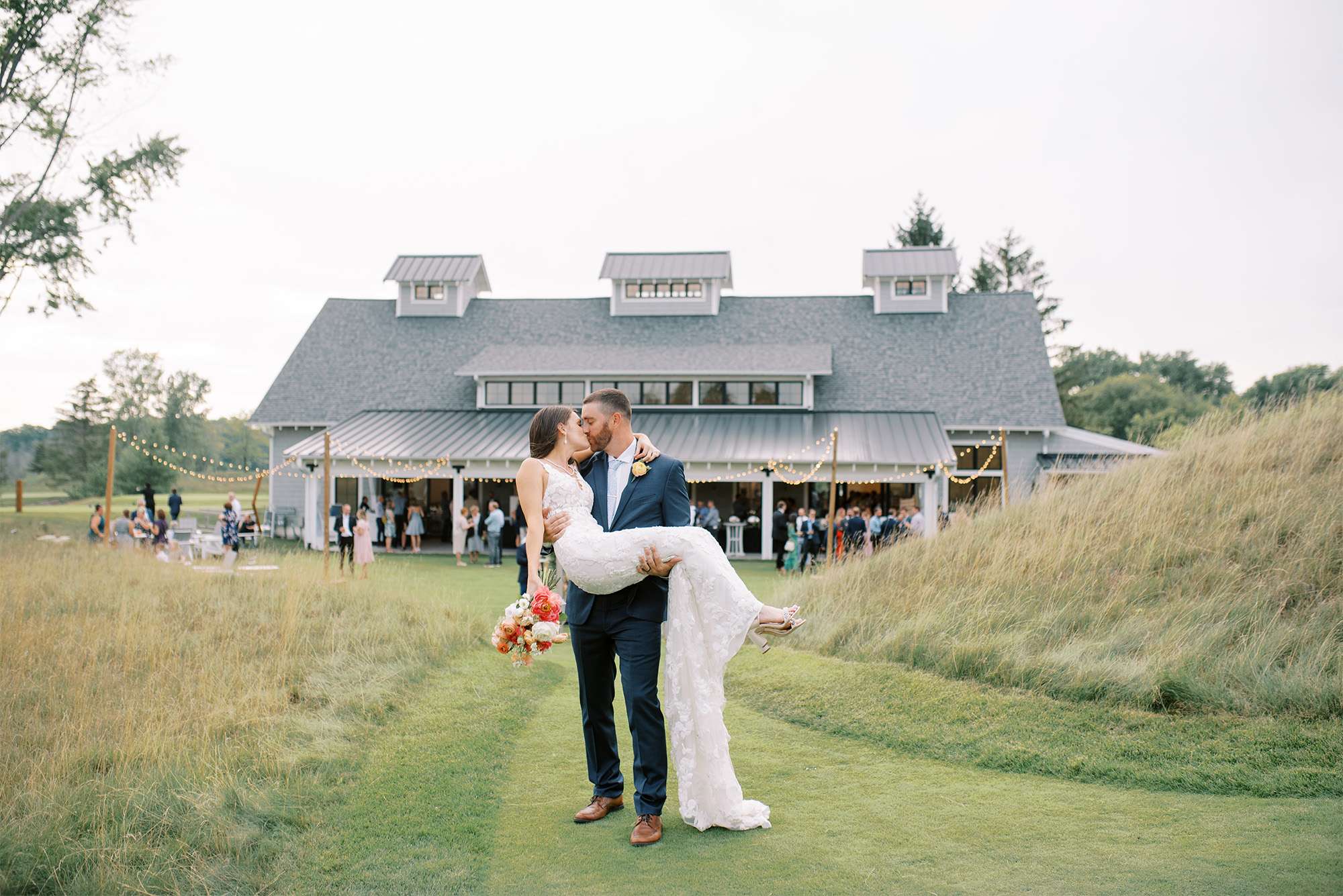 Groom holds and kisses bride with bouquet outside the Carriage House at the Club at Lac La Belle.