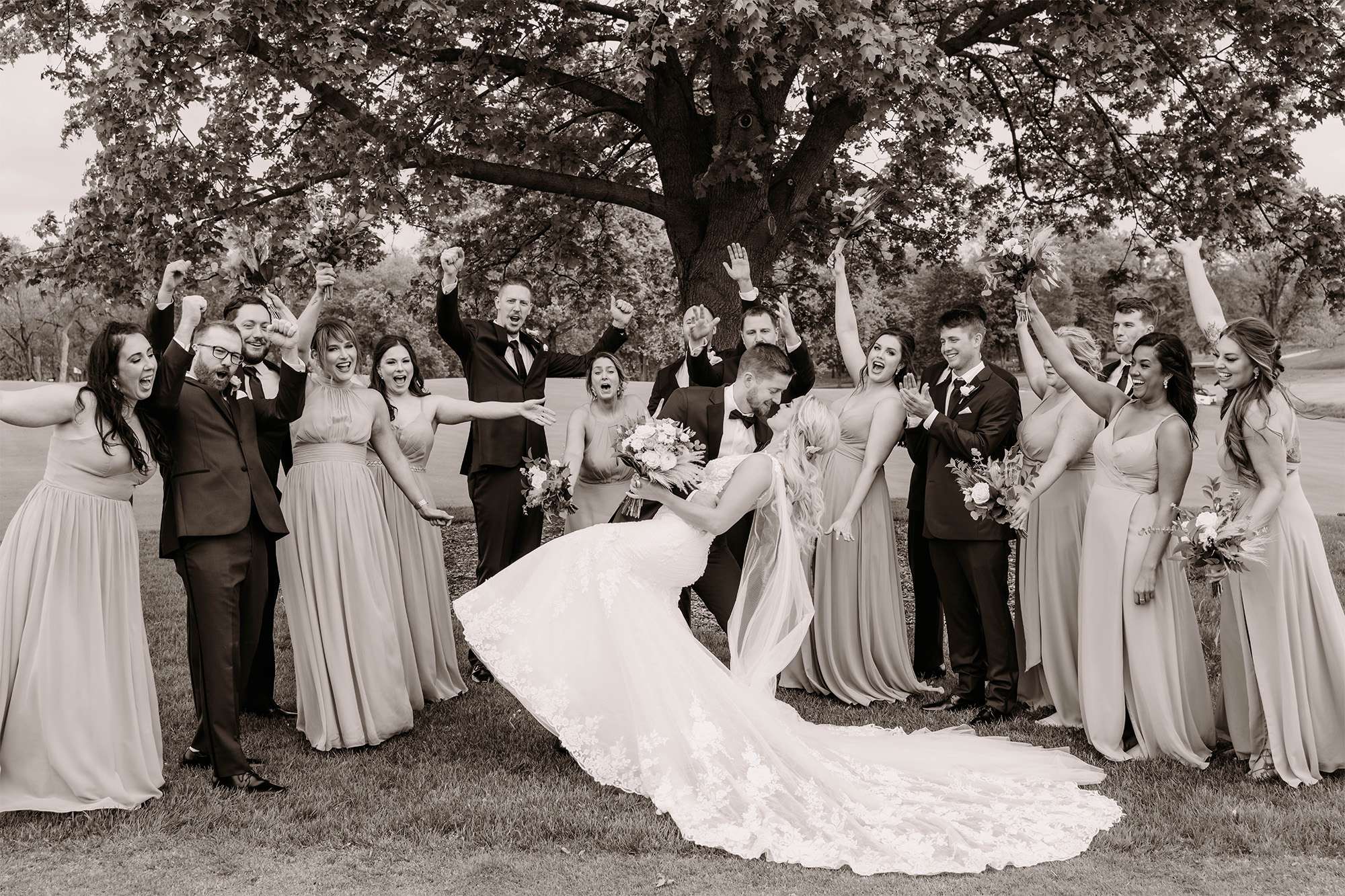 Groom dips bride while wedding party cheers at the Carriage House at the Club at Lac La Belle.
