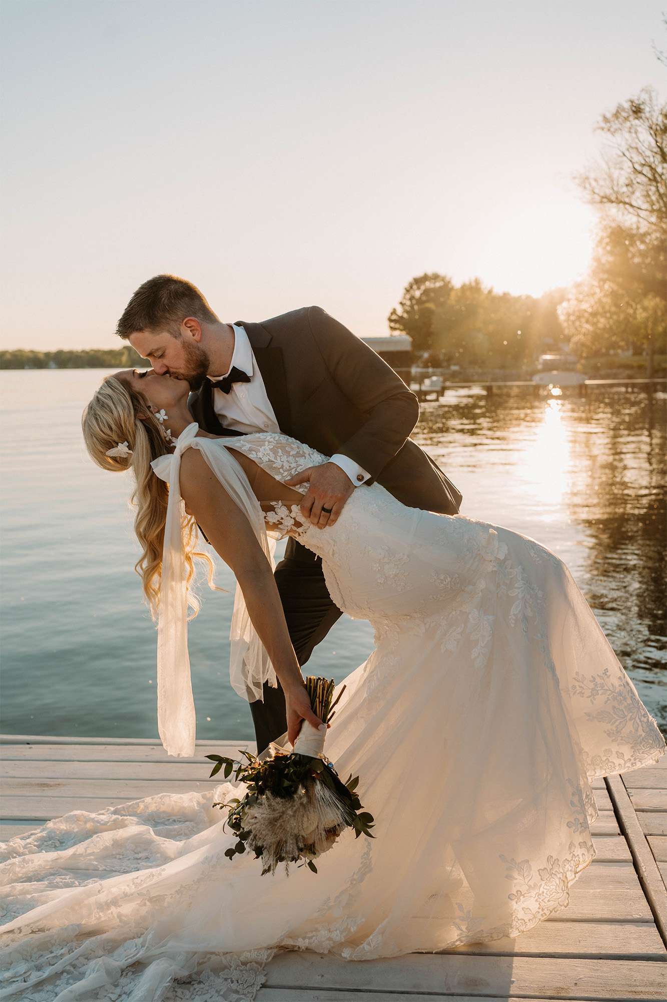Groom dips and kisses bride on pier.