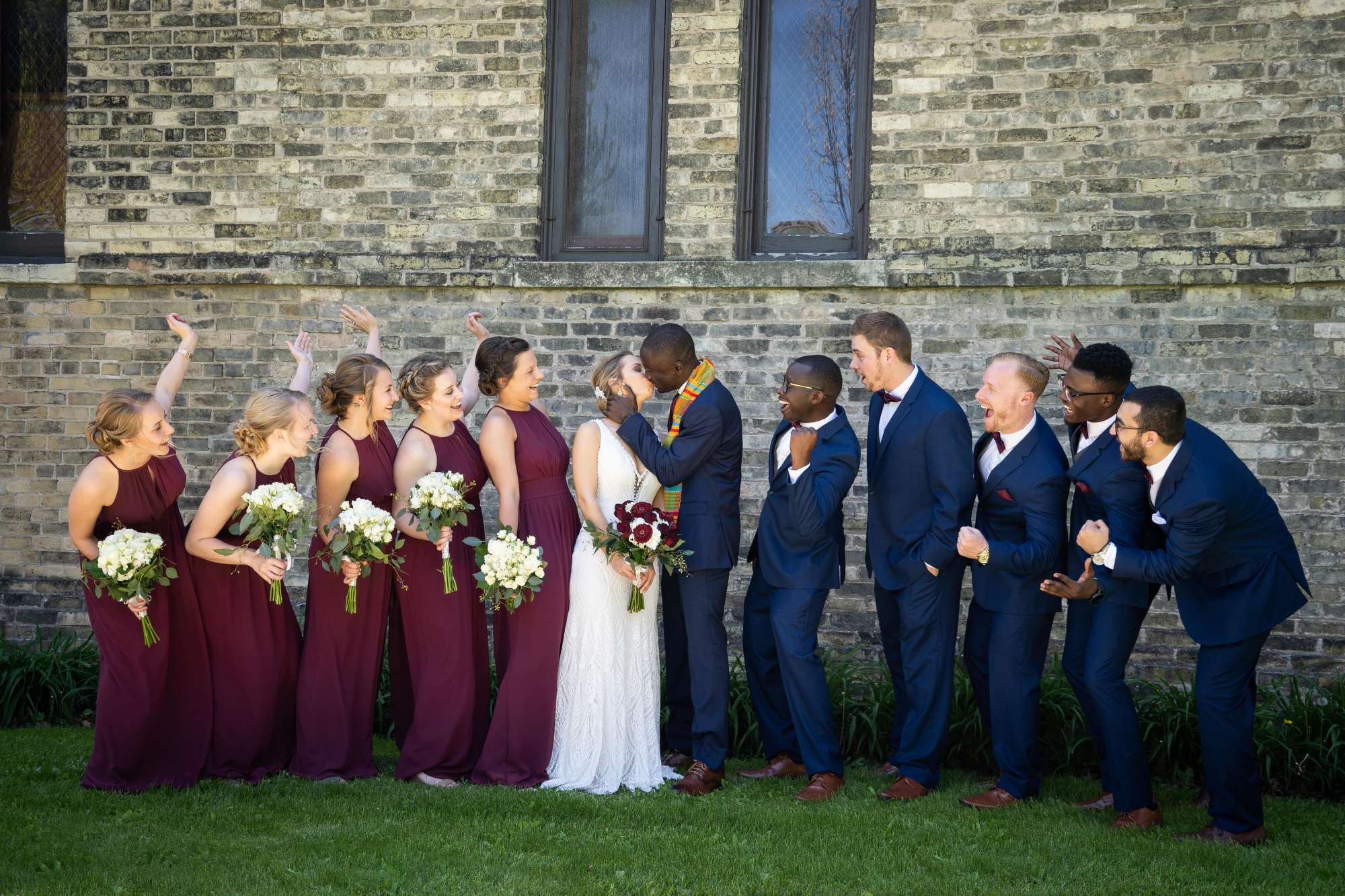 Groom kisses bride as wedding party looks on