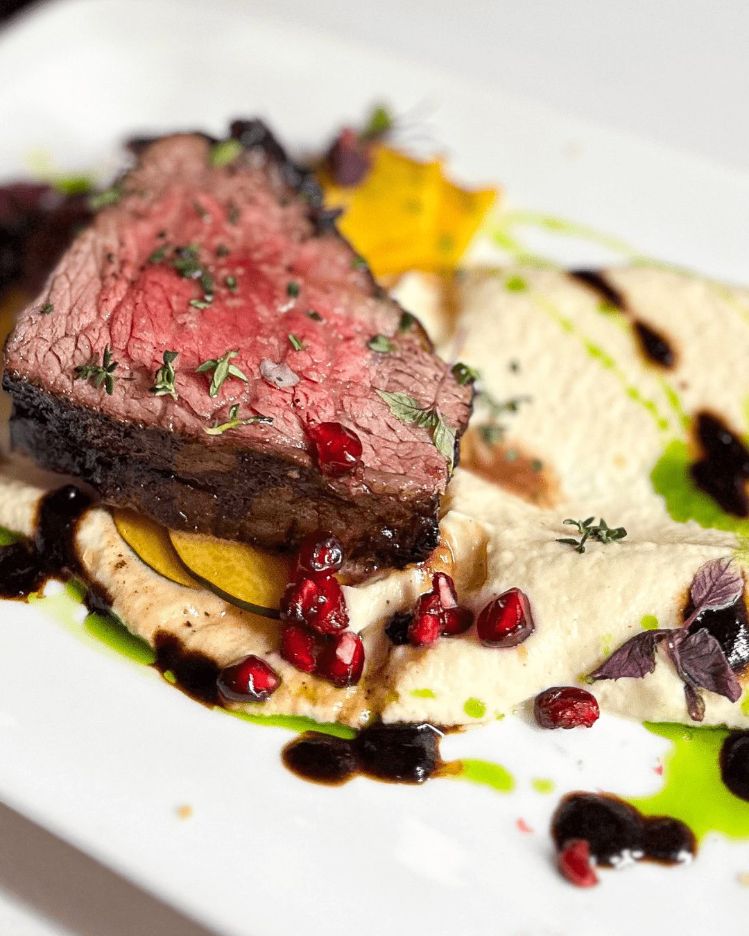 A beautifully plated steak entrée with pomegranate reduction and root vegetable purée by Noble Catering.