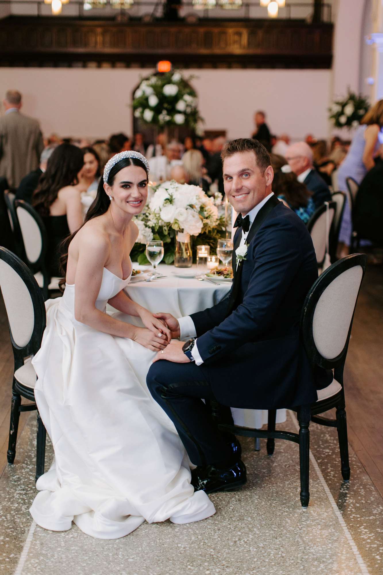 bride and groom hold hands at head table with chivaree chairs and floral by noble catering and events