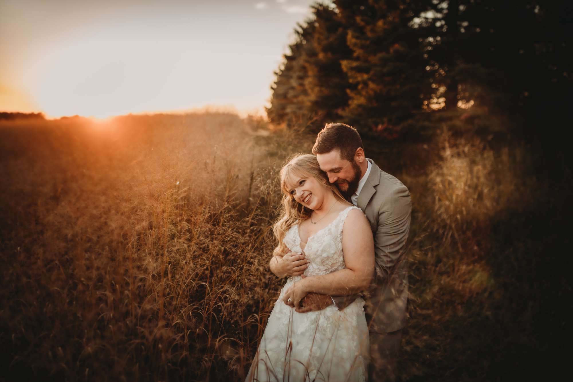 A newlywed couple shares an intimate embrace in the golden fields of Milford Hills at sunset, radiating love and warmth in the soft evening glow.