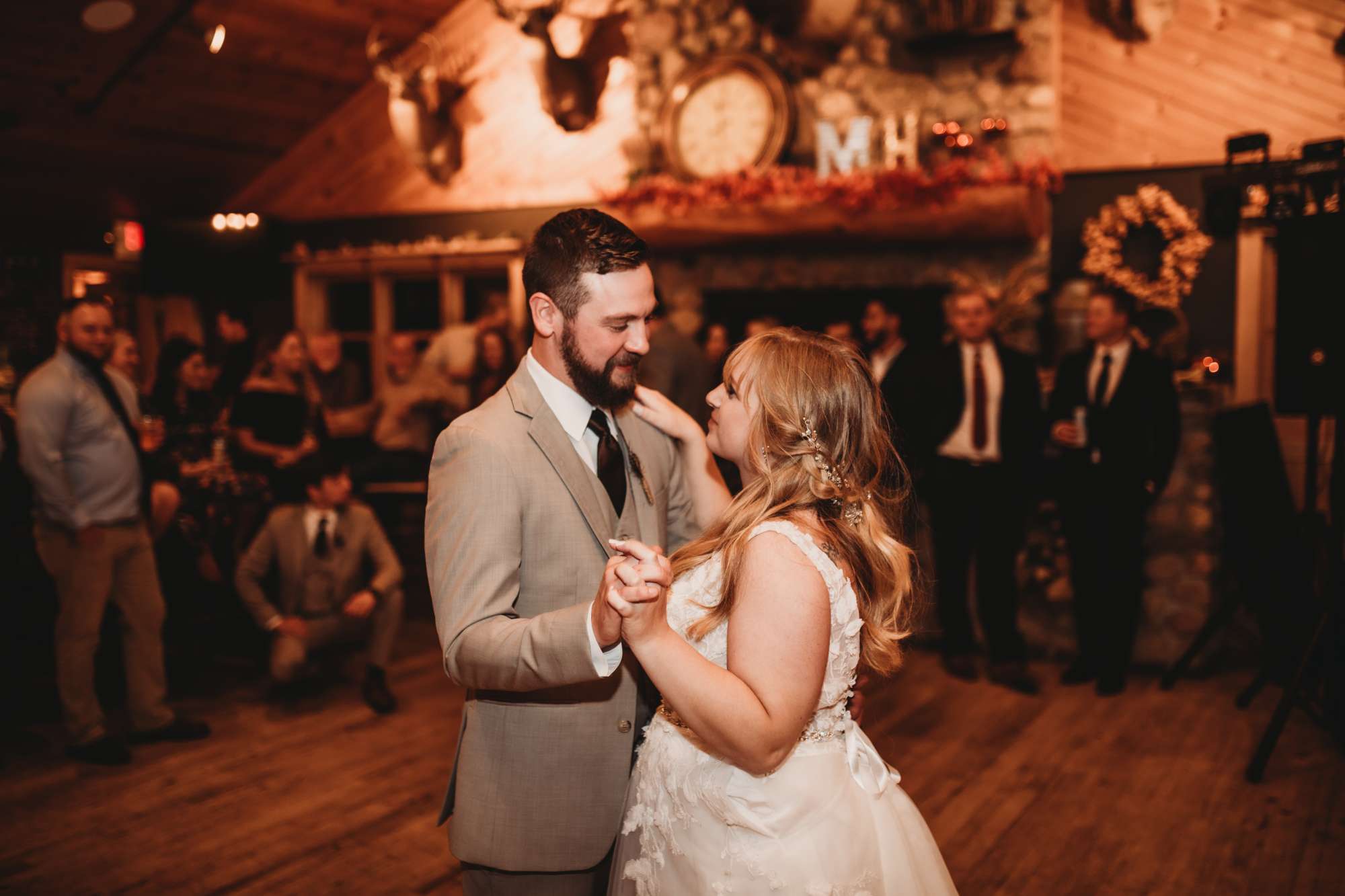 The bride and groom share a heartfelt first dance at Milford Hills, surrounded by loved ones in the warmly lit rustic reception hall.