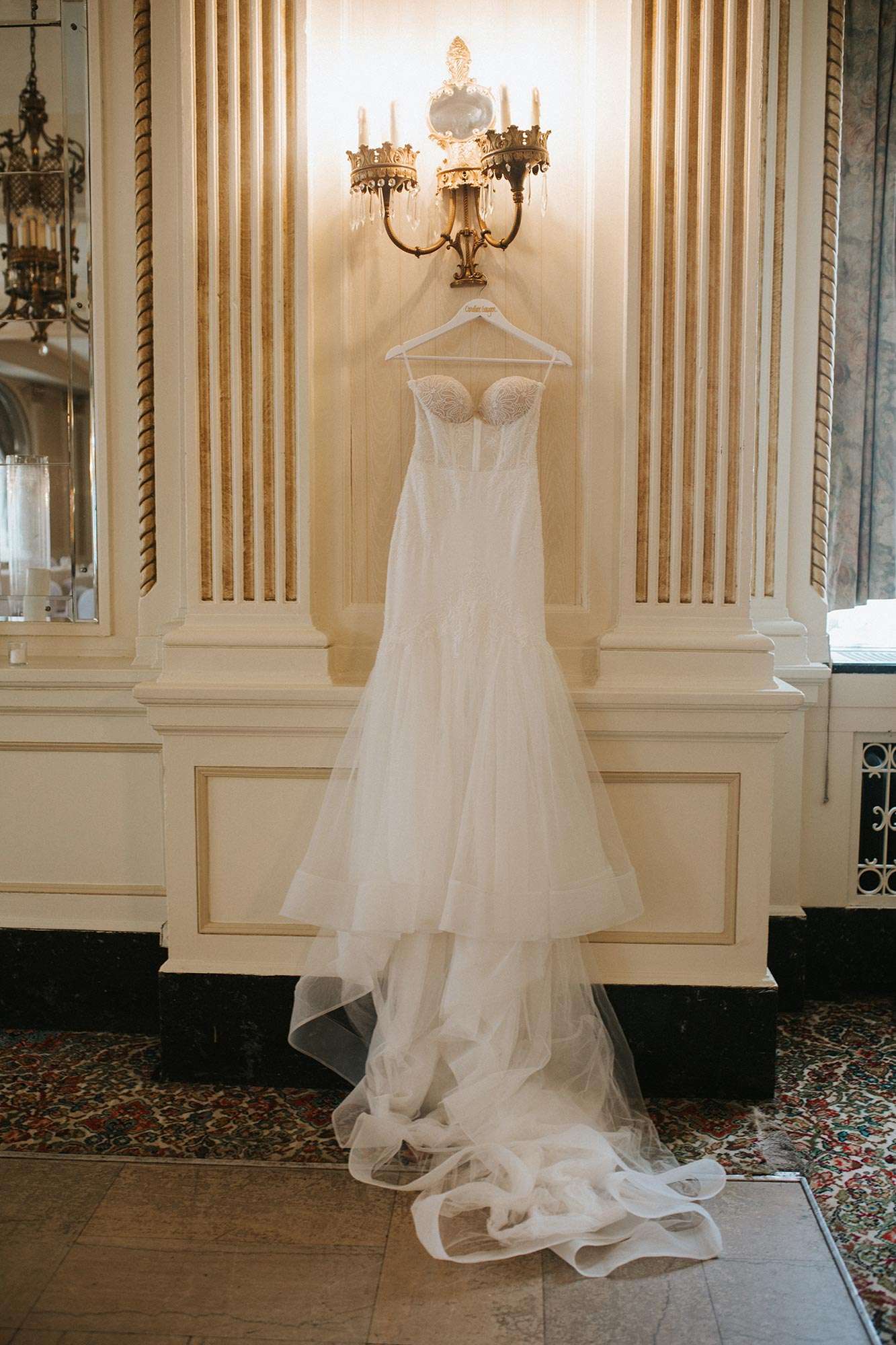 Caroline's bridal dress from Amelishan Bridal hangs on a wall sconce