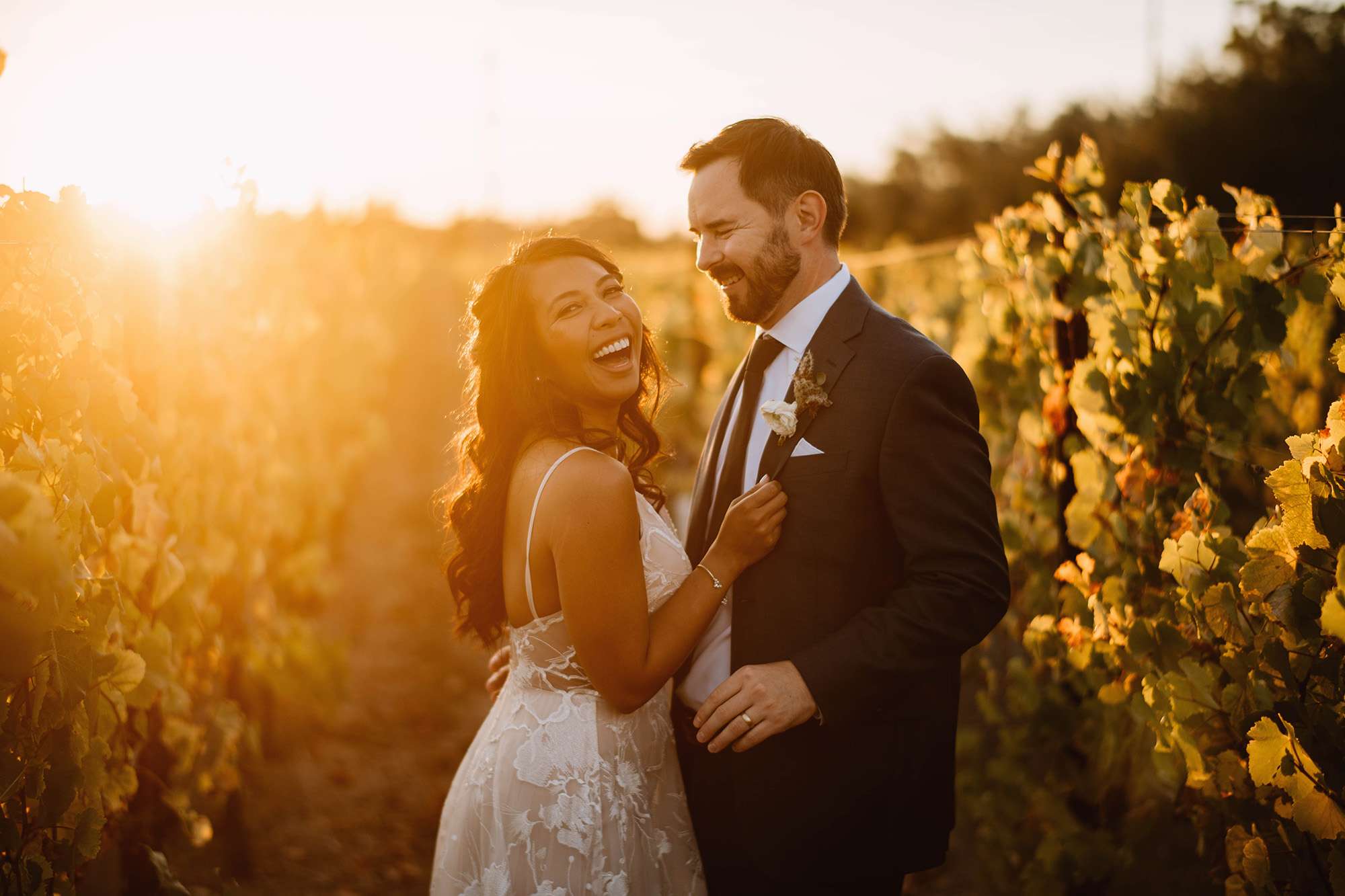 Bride and groom happily pose at sunset in field.
