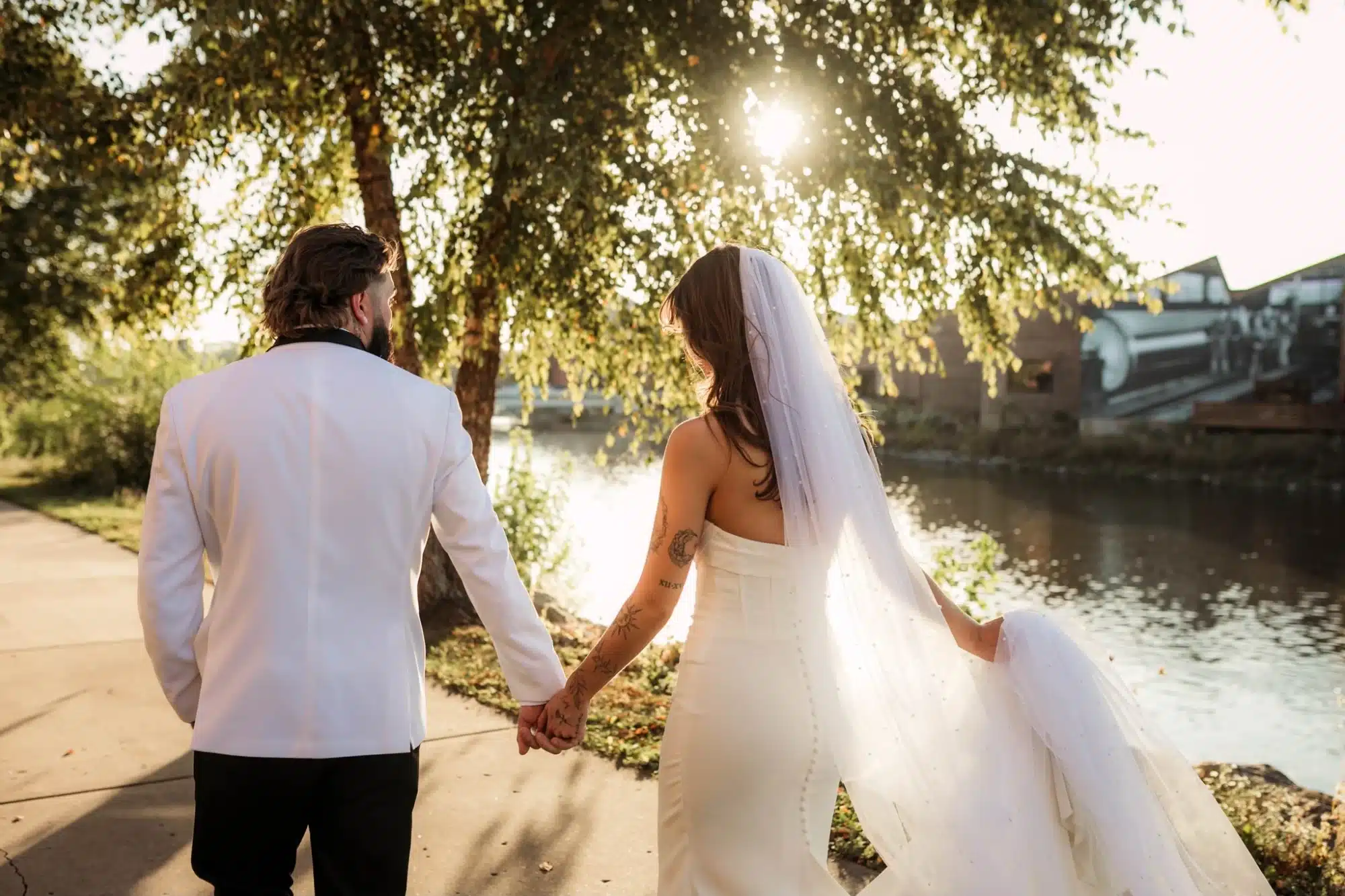 Bride and groom walk along the grounds and river of Ironworks Hotel Beloit