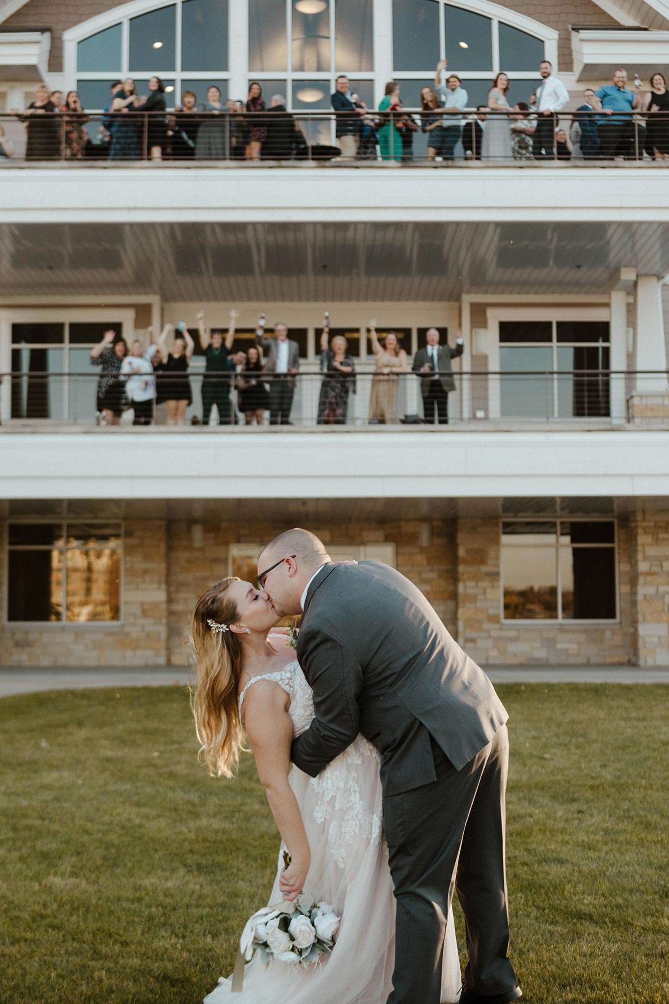 groom dipping bride for a kiss with guests cheering from Oconomowoc Community Center balconies