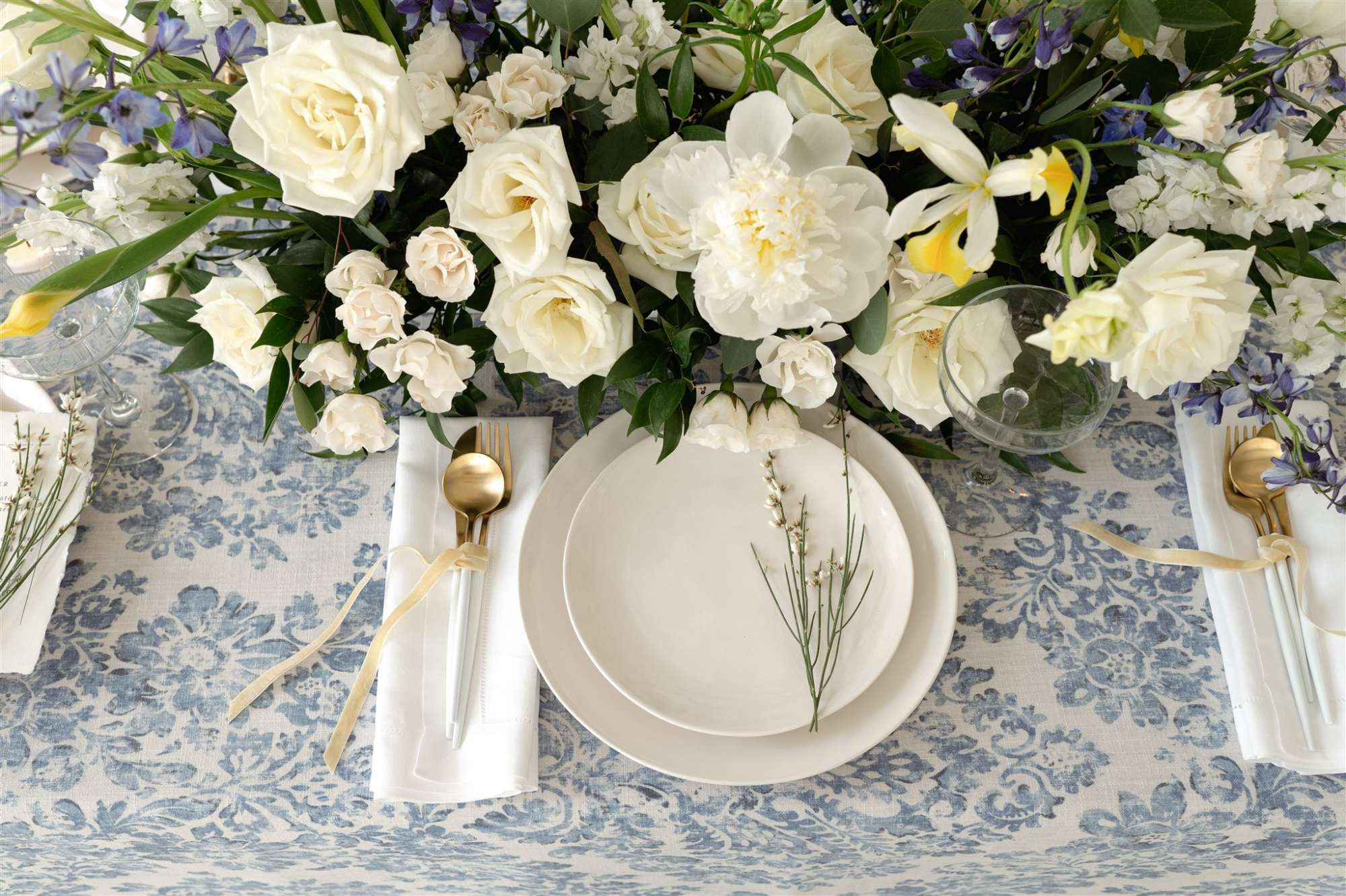 Feisty-Flowers-floral-centerpiece A lush Feisty Flowers floral centerpiece of white roses and delicate blooms arranged against a blue-patterned table setting.