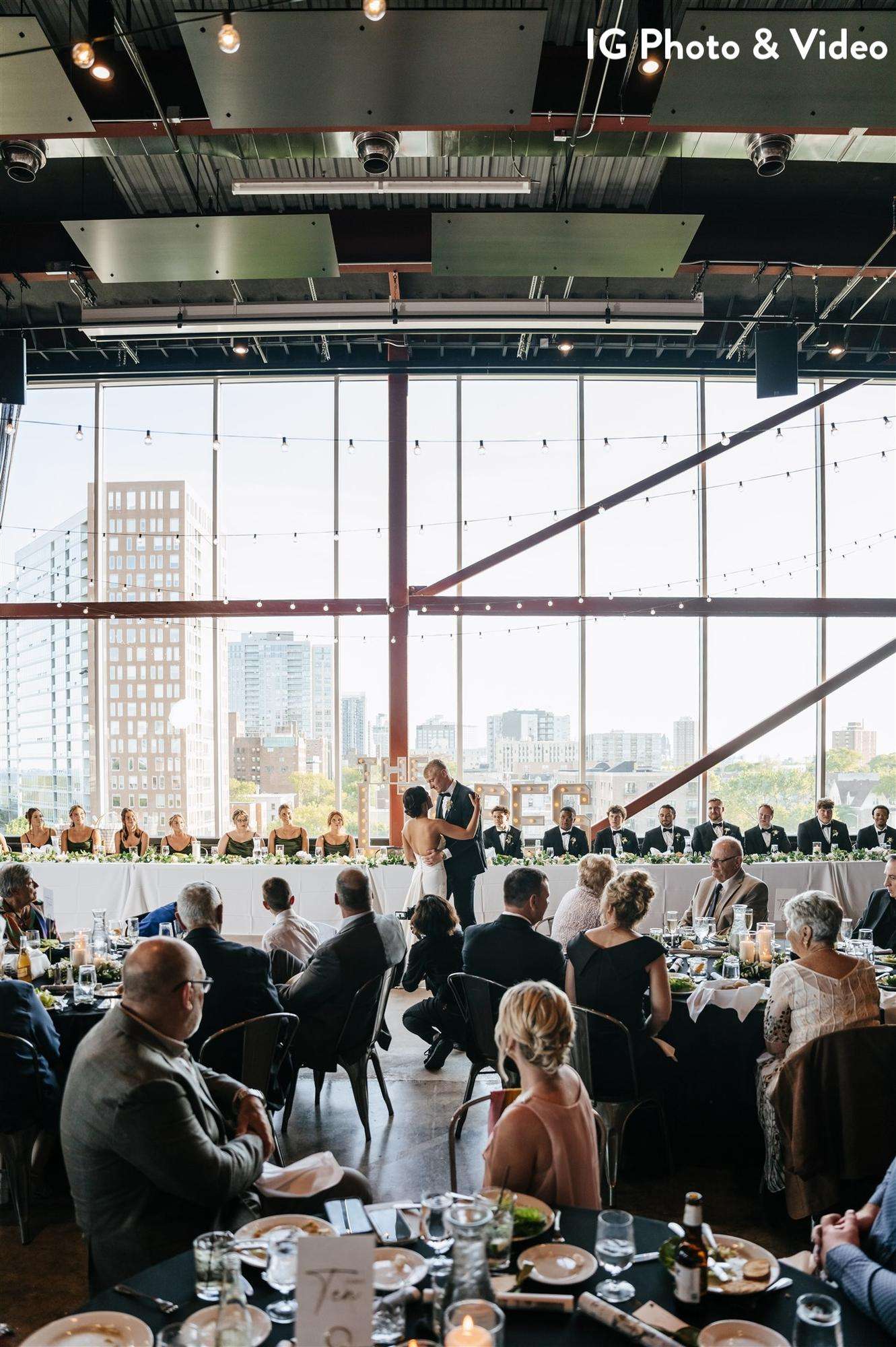 A wedding reception at Jan Serr Studio features a head table with a city skyline backdrop, capturing a couple’s first dance.
