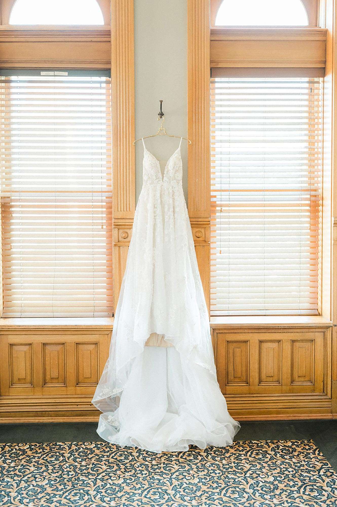 Lace detailed wedding gown from Vera's Bridal hanging between windows