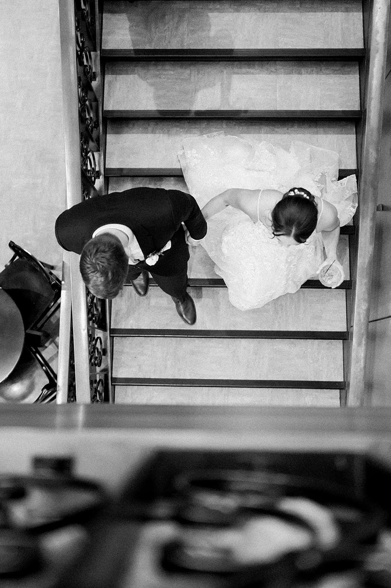 Aerial view of couple descending stairwell with black ornate railing holding hands