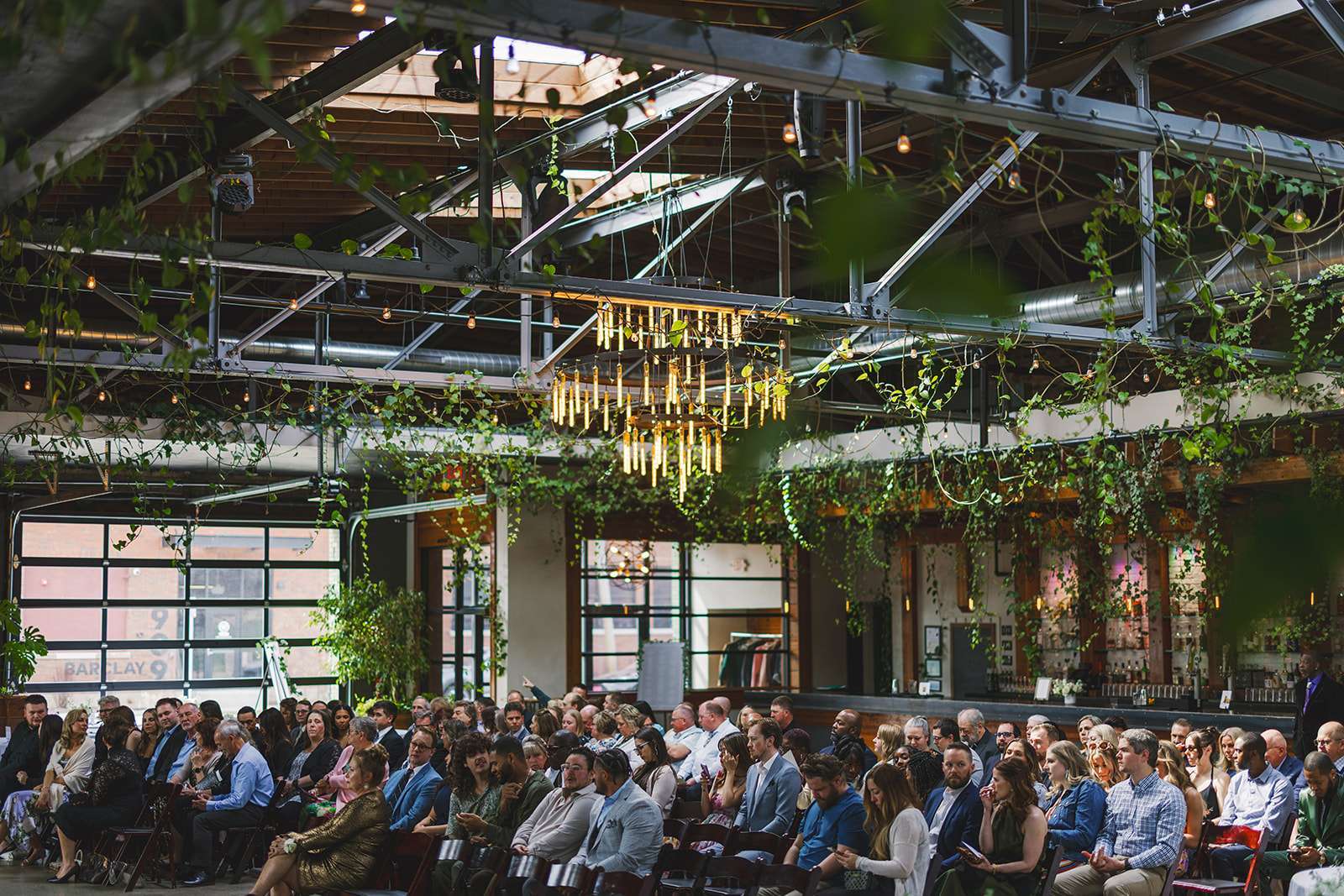 20250419_14_28_51 Guests gather beneath cascading vines and glowing chandeliers inside The Ivy House, ready to witness a beautiful wedding ceremony.