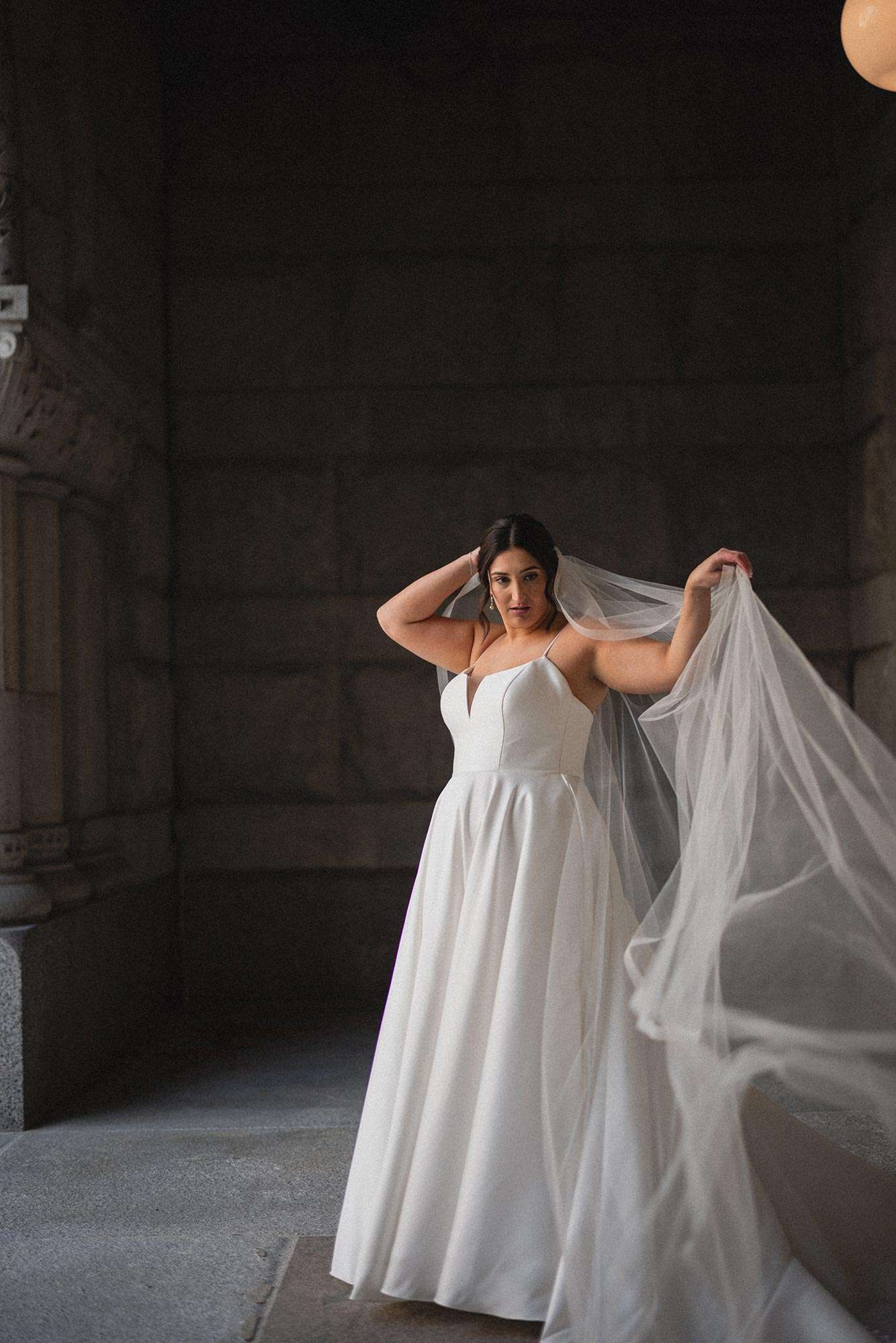 Bride holding out veil wearing classic white spaghetti strap dress with v-neck plunge