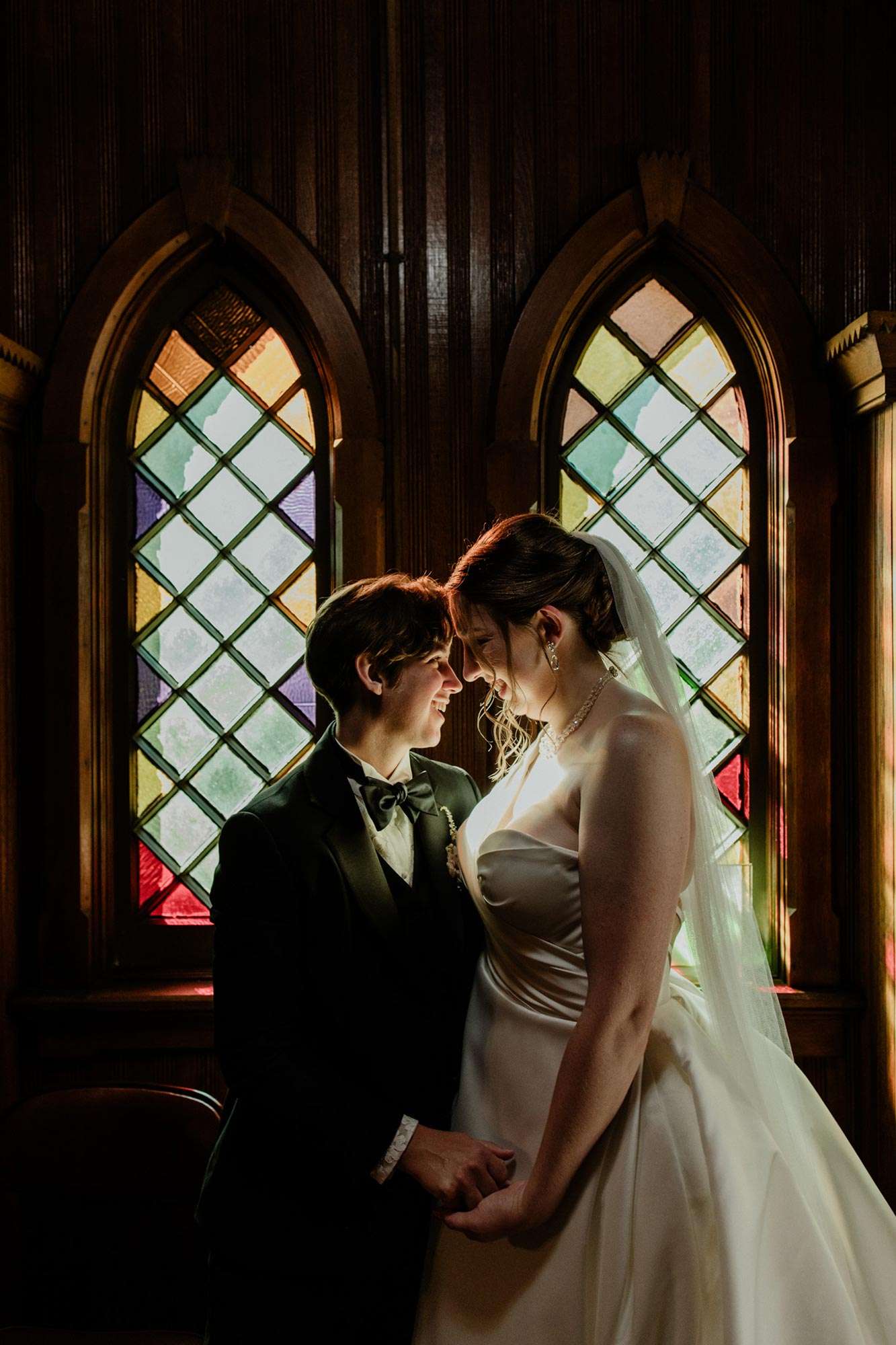 couple with foreheads together in front of stained glass windows as sun shines through