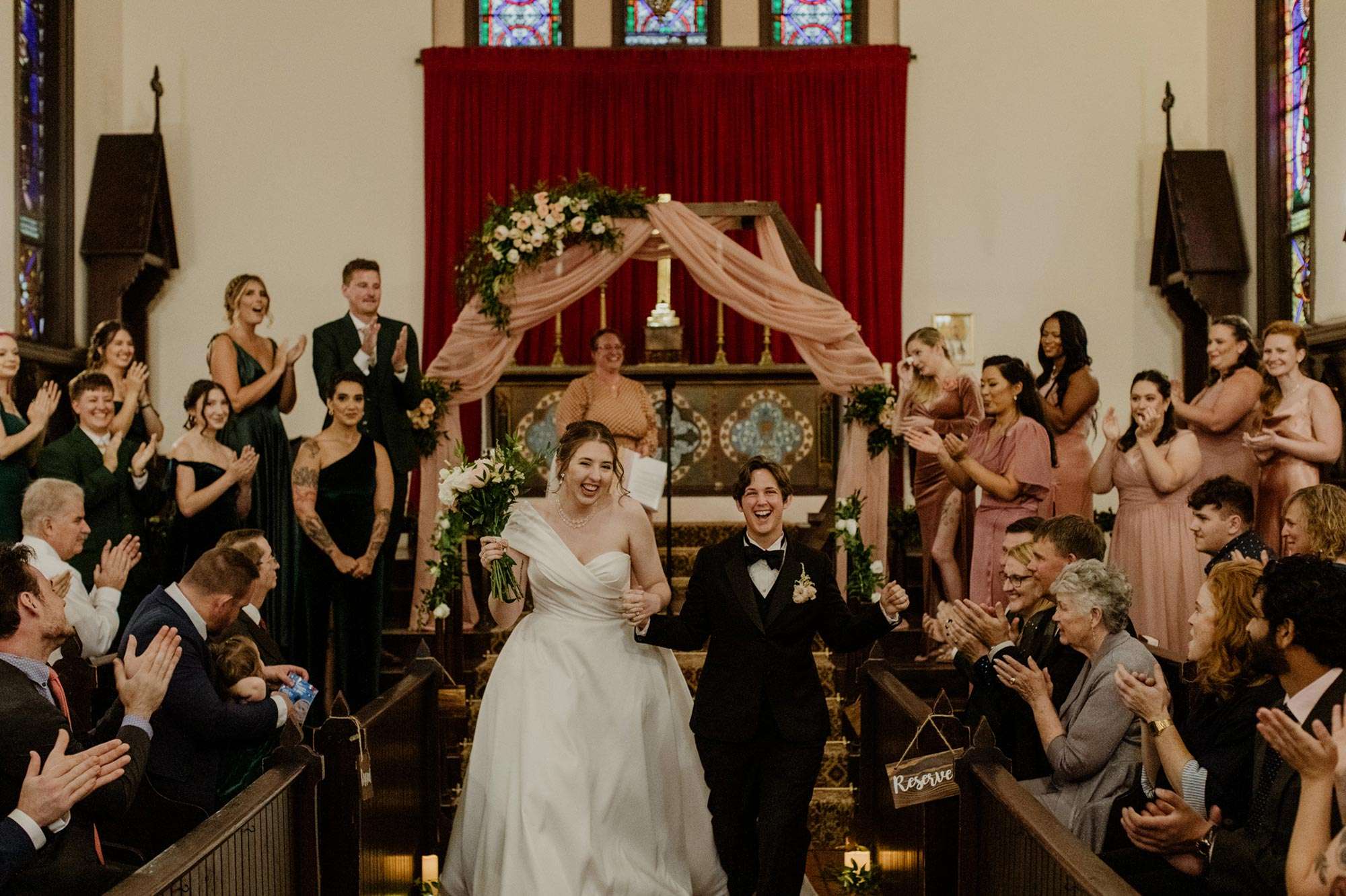 couple laughing as they walk down aisle during recessional while guests and wedding party clap
