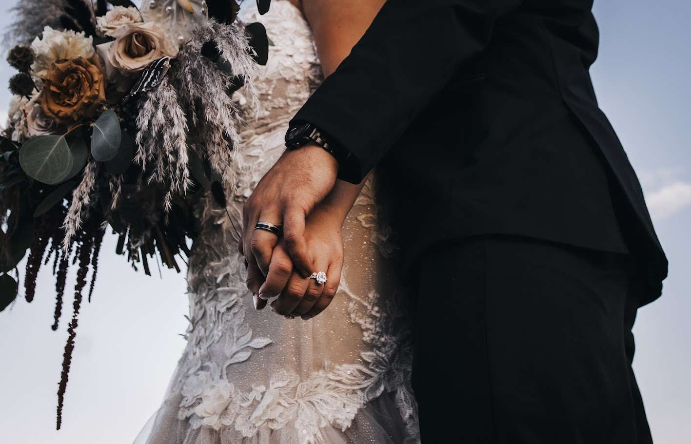 Close up photo of bride and grooms hands and their wedding rings. Her dress and bouquet creating a backdrop.