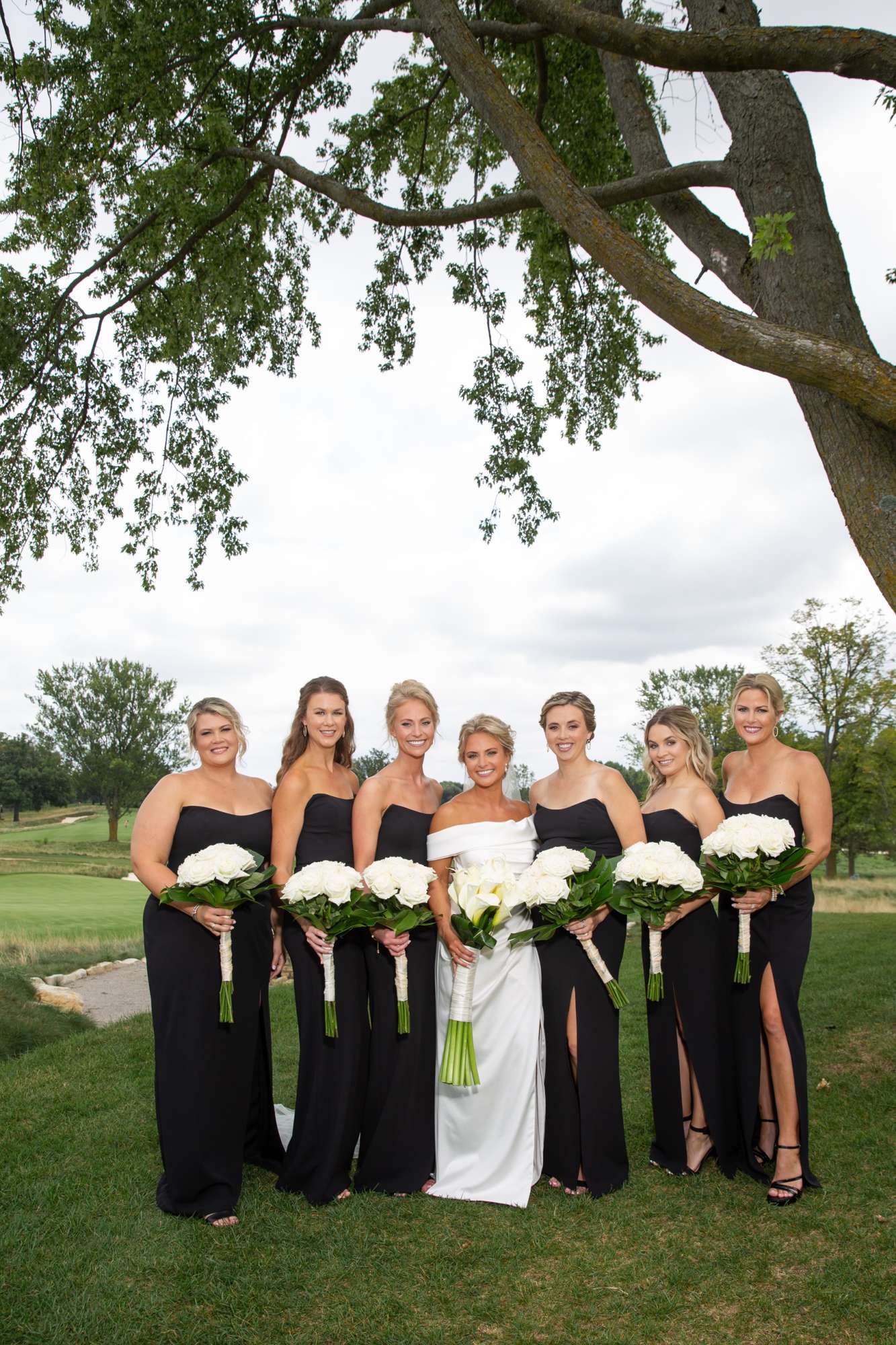 Bridal party outside. Bridesmaids wearing black strapless long dresses and white bouquets and bride in off the shoulder dress with lillys. Bridal party outside. Bridesmaids wearing black strapless long dresses and white bouquets and bride in off the shoulder dress with lillys.