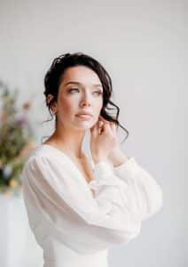 Bride looking off in a white wedding gown with flowy sleeves putting in hear earring. Bride looking off in a white wedding gown with flowy sleeves putting in hear earring.