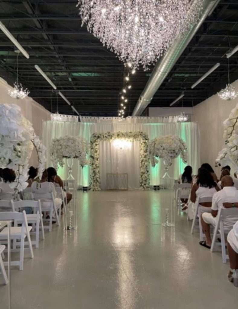 Ceremony space at The Mitch, adorned with a stunning crystal chandelier, elegant drapery, and floral archway.