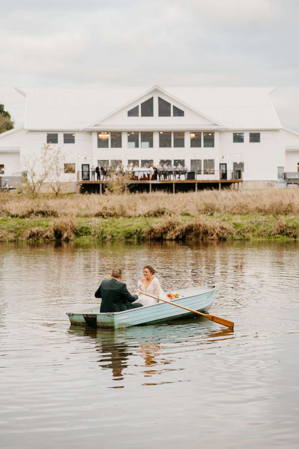 Bride and groom in rowboat on the pond next to fete in wales, wi. fête