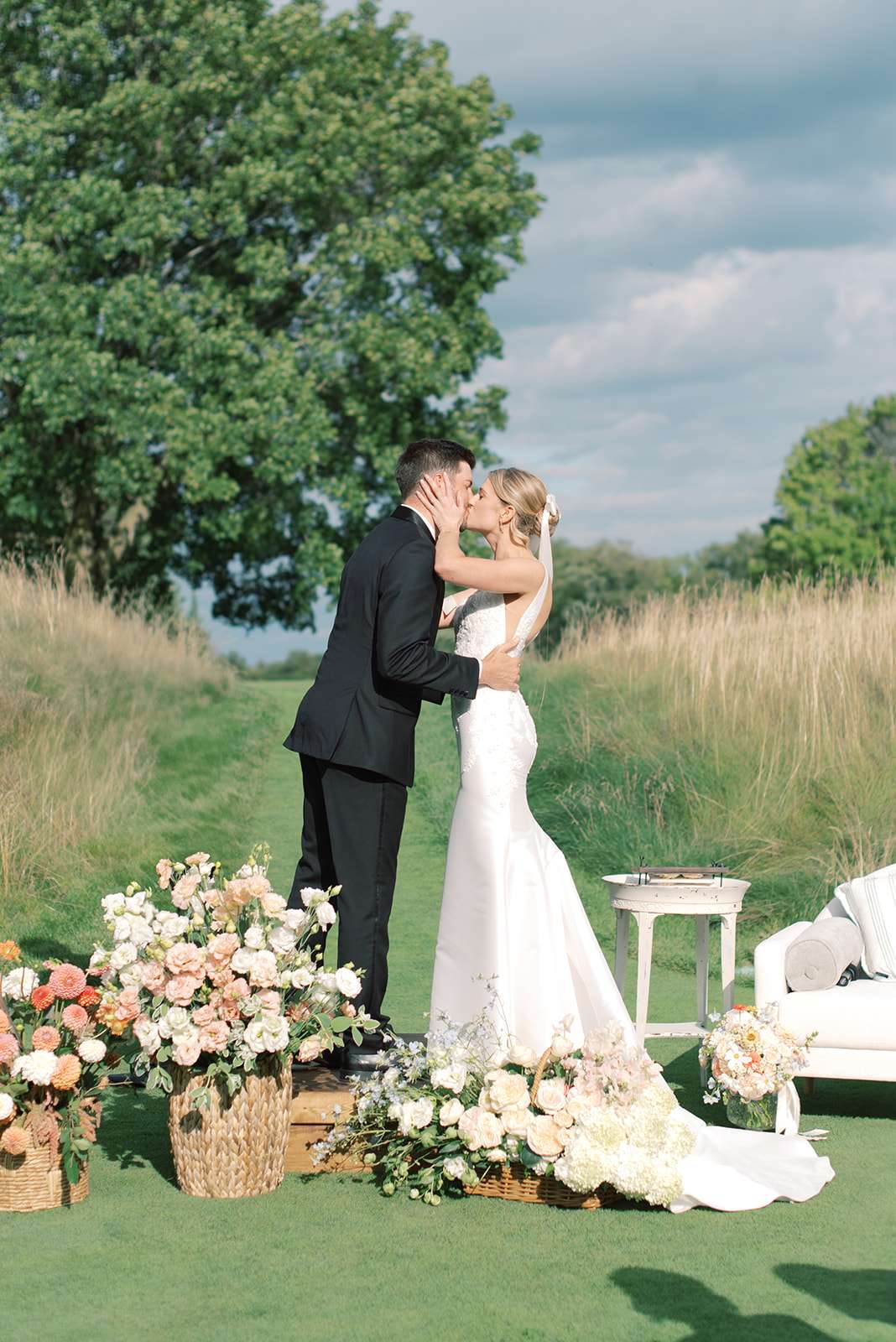 Bride and groom kissing at the wedding ceremony location at The Carriage House surrounded by flowers. Bride and groom kissing at the wedding ceremony location at The Carriage House surrounded by flowers.