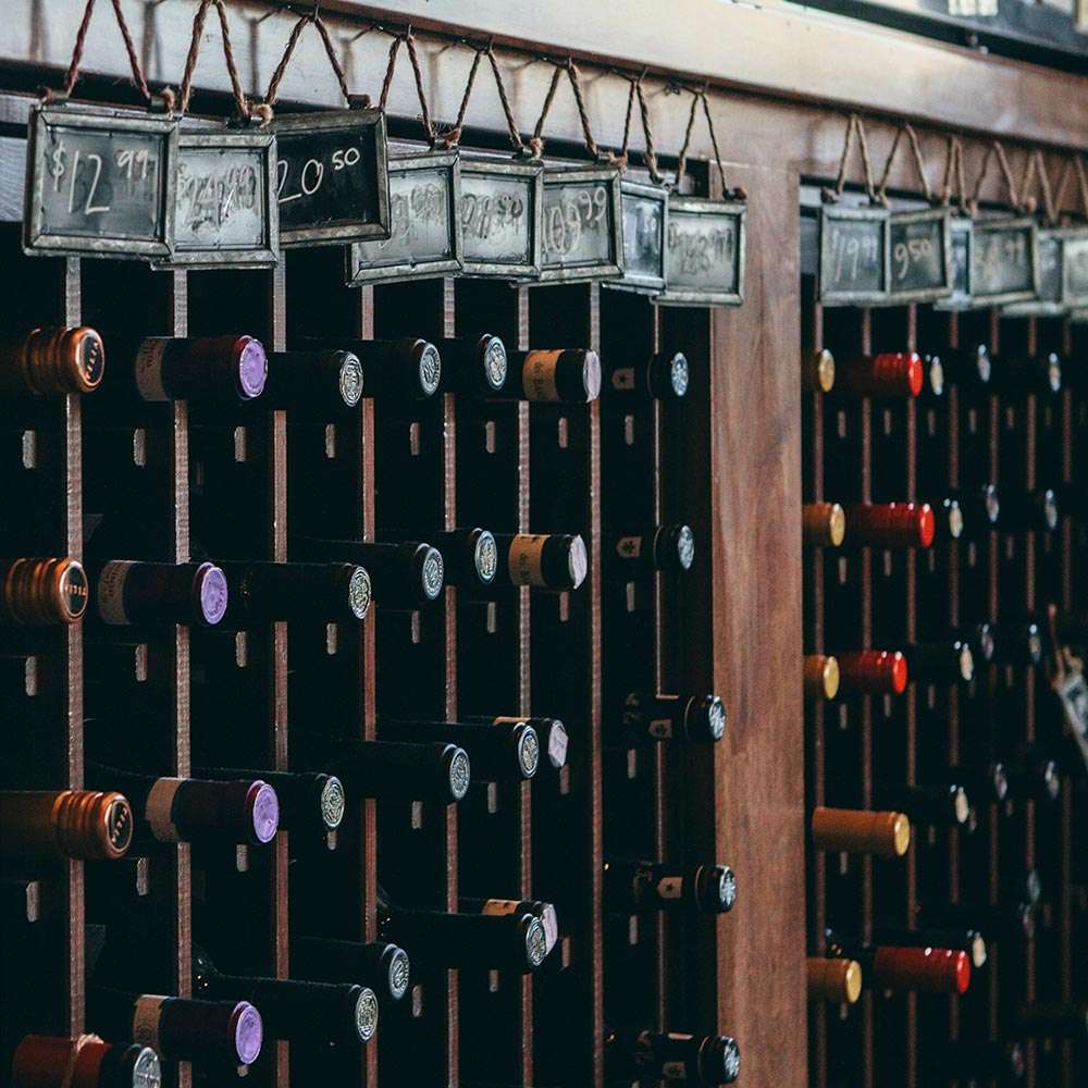 Close-up of The Ruby Tap's wine rack, displaying rows of wine bottles in rustic metal frames above each slot.