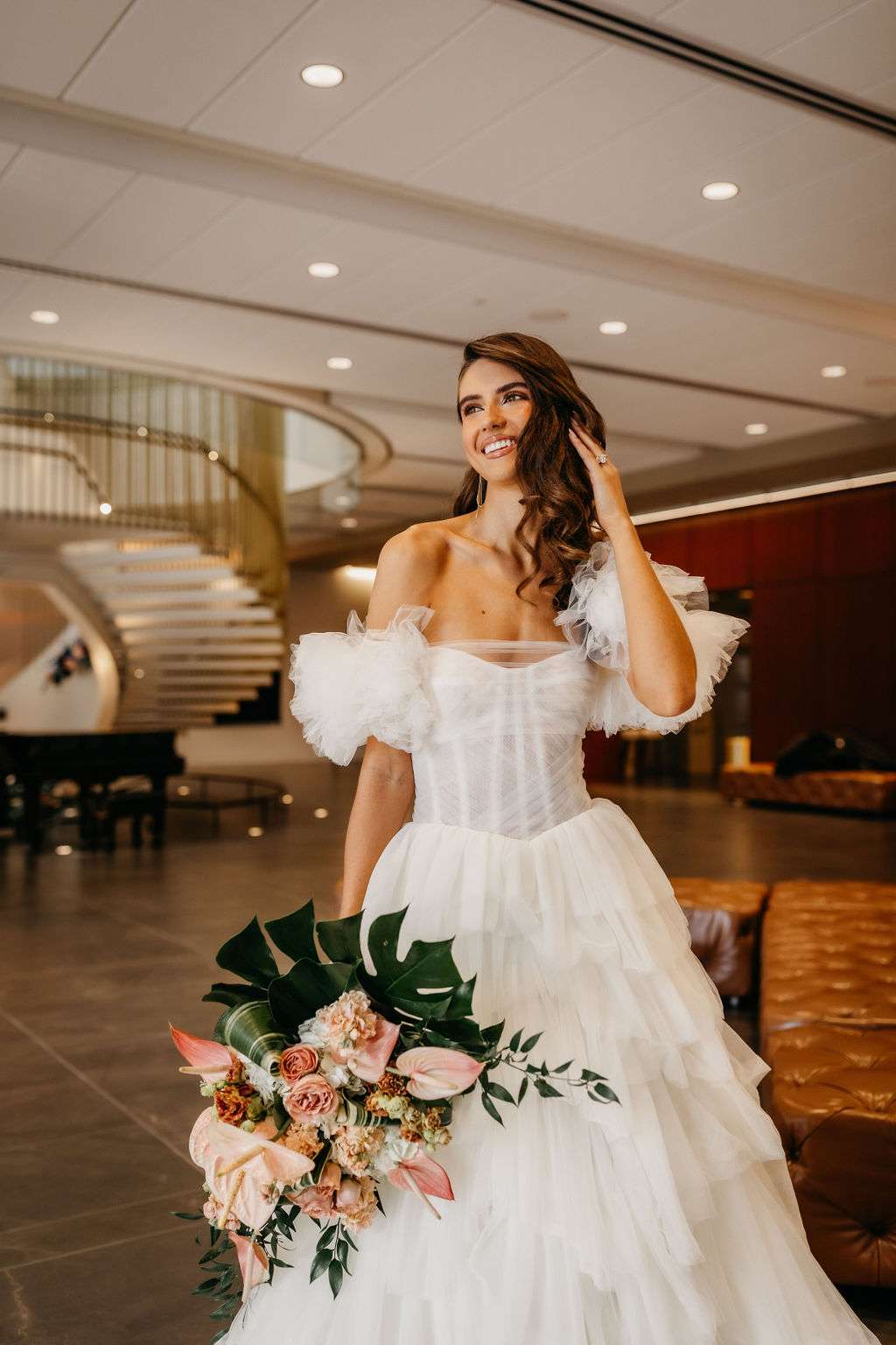 Bride with tulle dress and corset bodes and off the shoulder puff sleeves, holding large tropical wedding bouquet by Belle Fiori. Bride with tulle dress and corset bodes and off the shoulder puff sleeves, holding large tropical wedding bouquet by Belle Fiori.