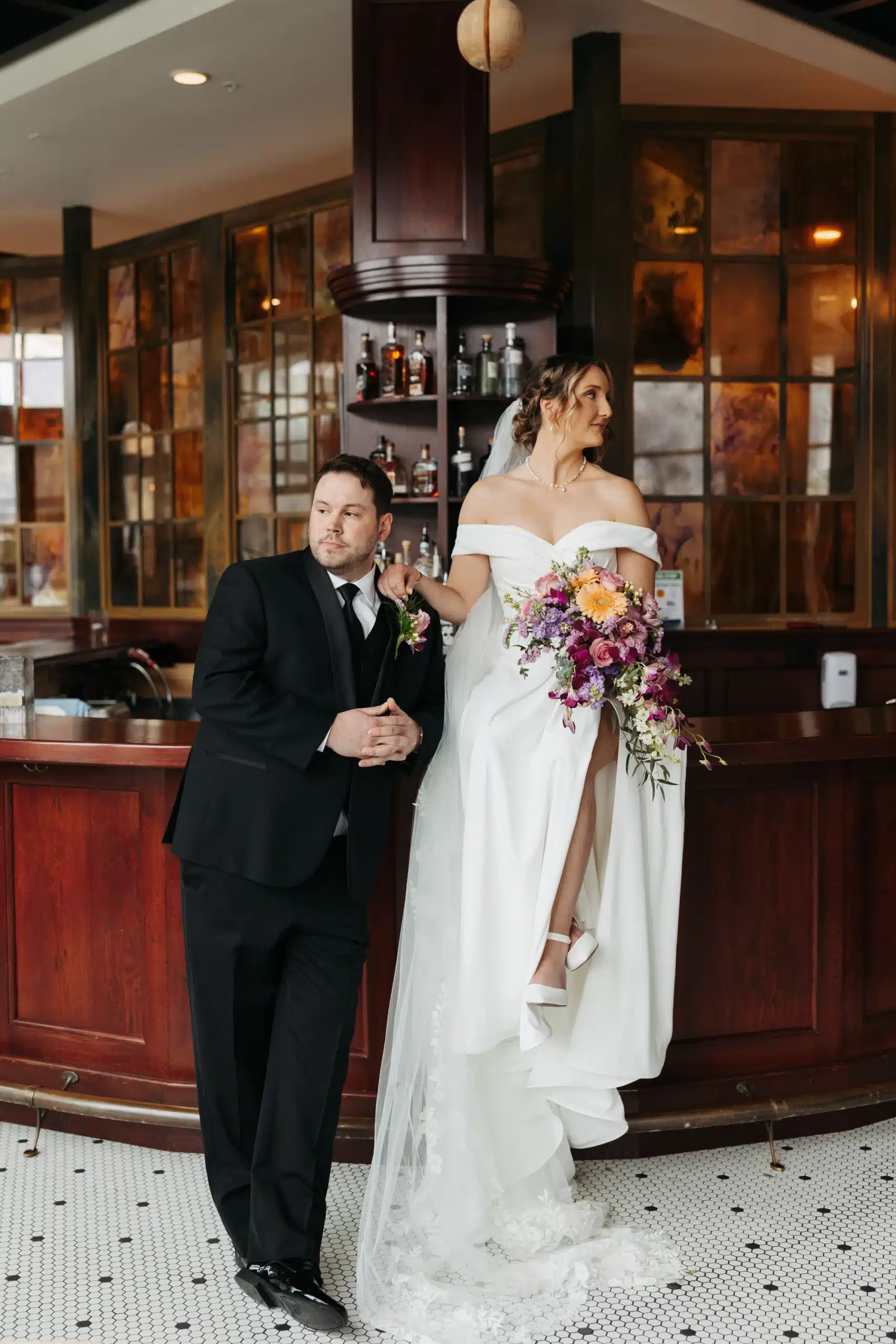 Bride sitting on the bar of Hotel Goodwin and her groom standing next to her.