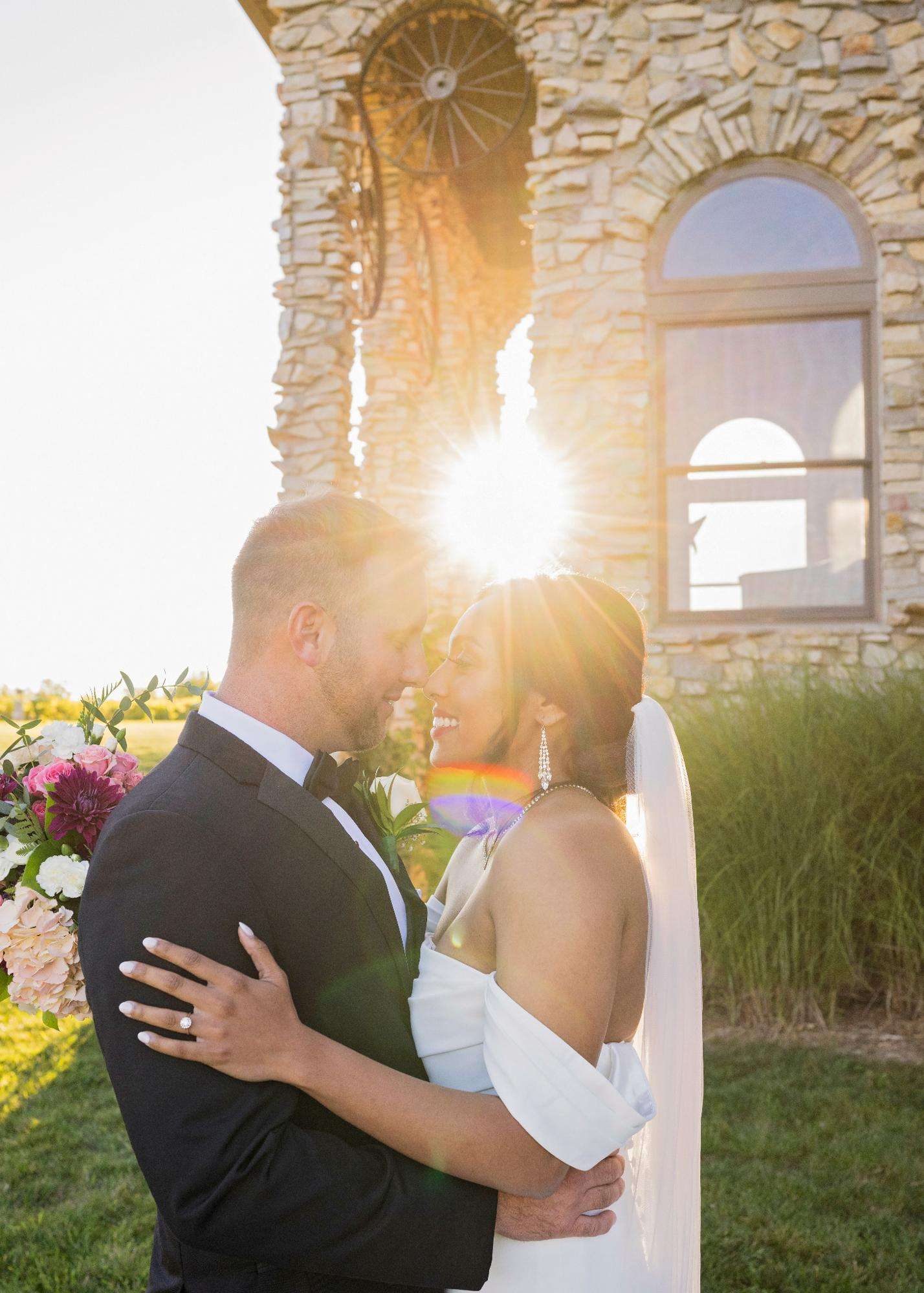 A glowing sunset highlights a joyful embrace between the bride and groom beside a rustic stone tower, captured by Allysha Noelle Photography.