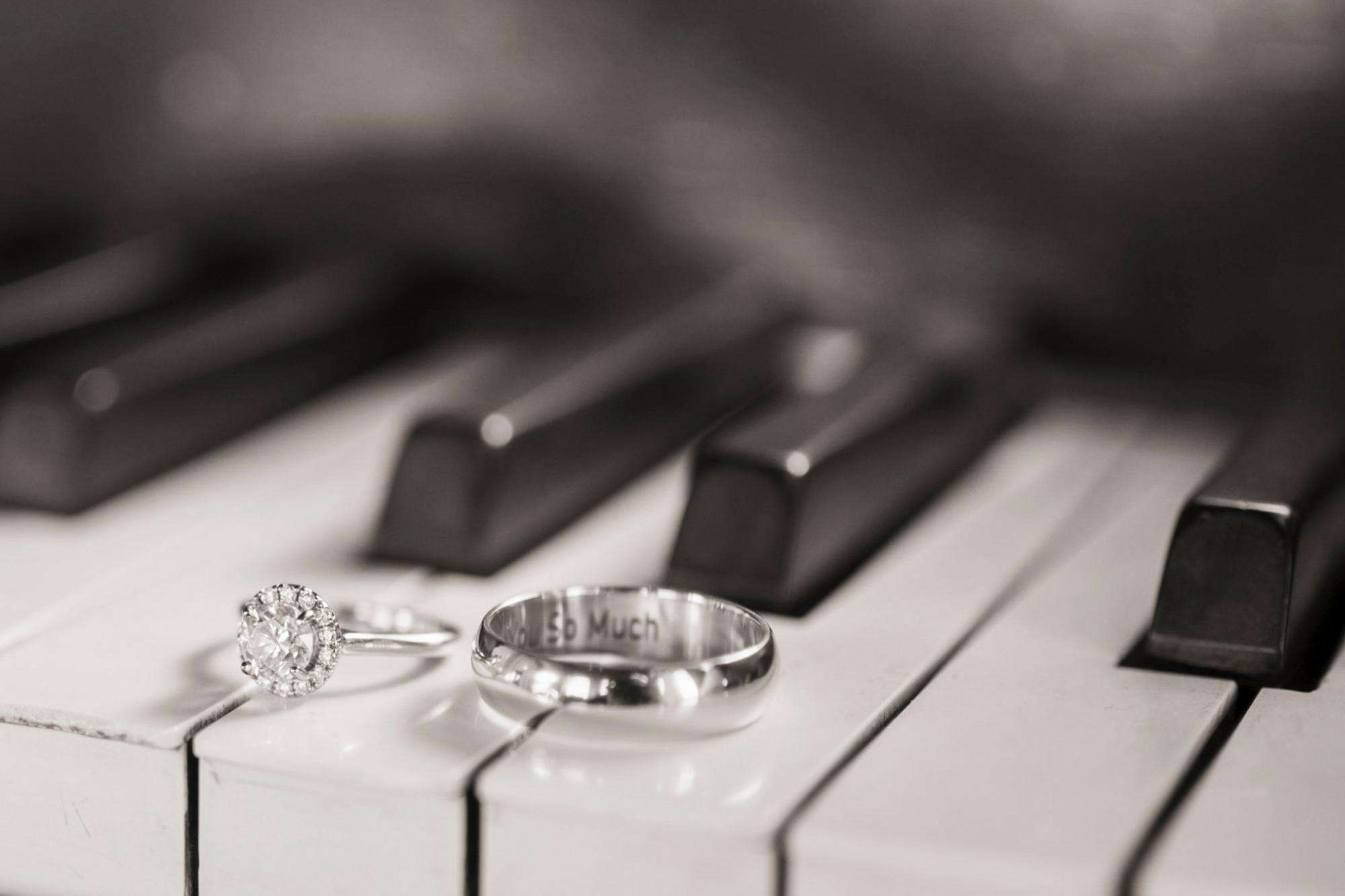 Wedding rings rest gently atop piano keys, one engraved with “So Much,” in this detailed shot by Allysha Noelle Photography.