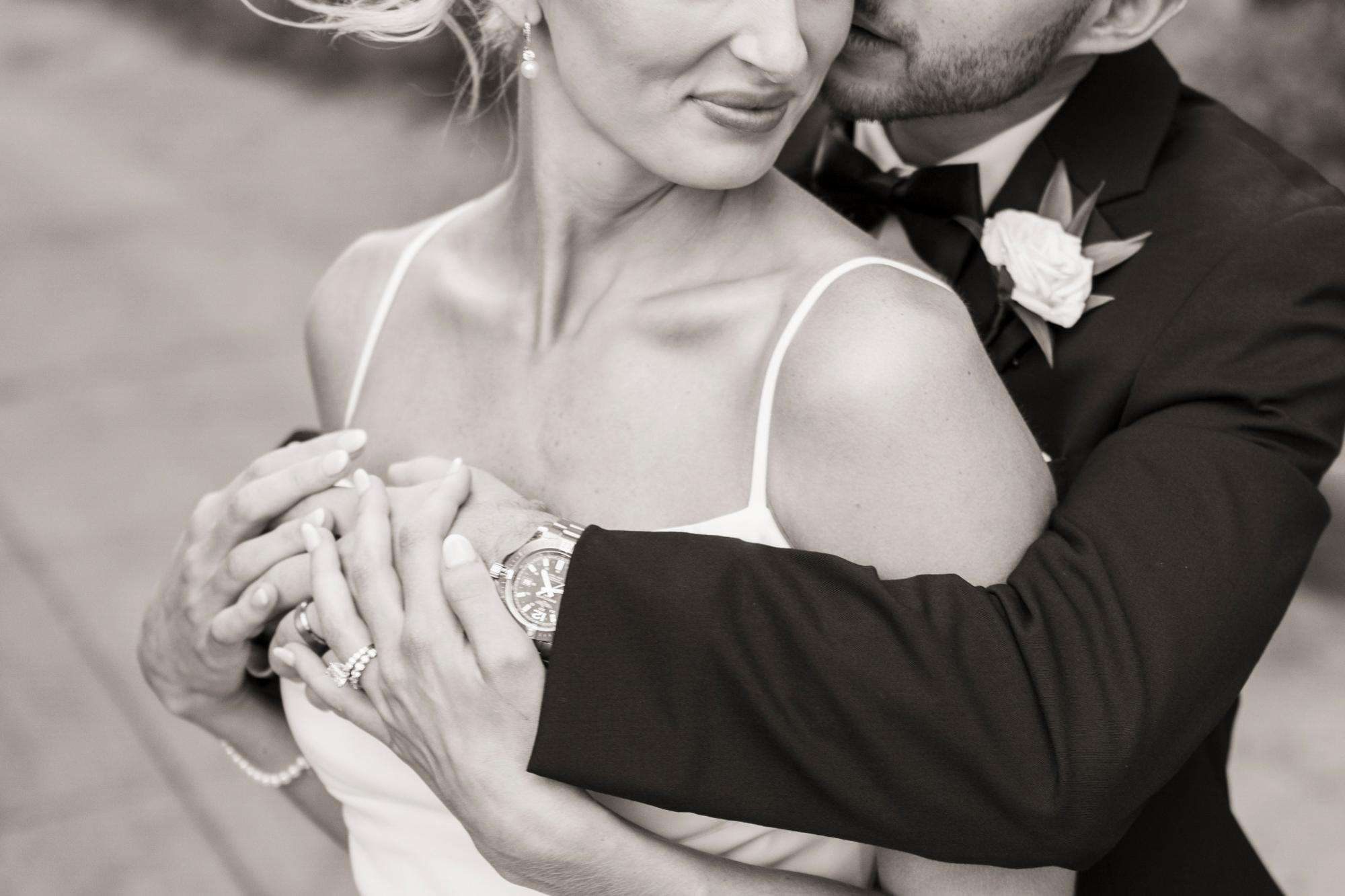 A black-and-white close-up of a groom holding his bride close, radiating elegance and intimacy by Allysha Noelle Photography.
