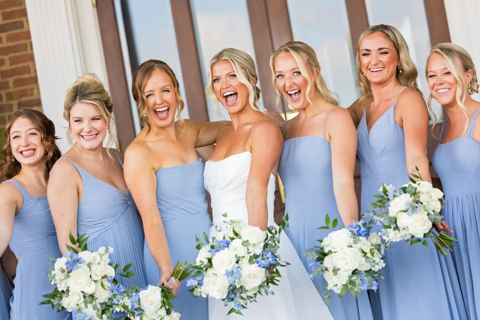 Bride with bridesmaids in blue dresses on the steps of the Delafield Hotel.
