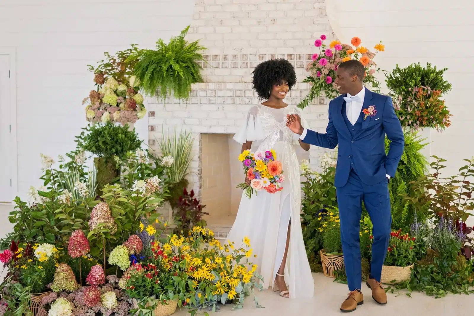 Bride and groom walking hand in hand surrounded by colorful flowers.