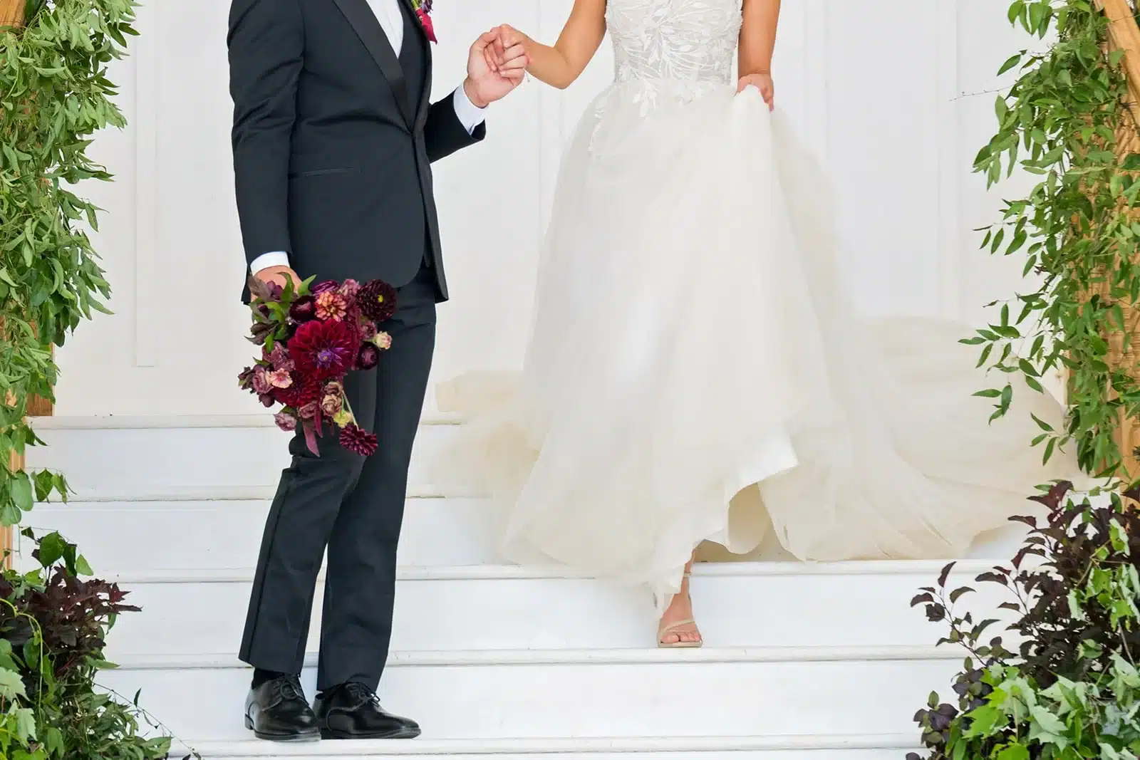 Bride and groom walking down stairs with navy suit and deep red bouquet.