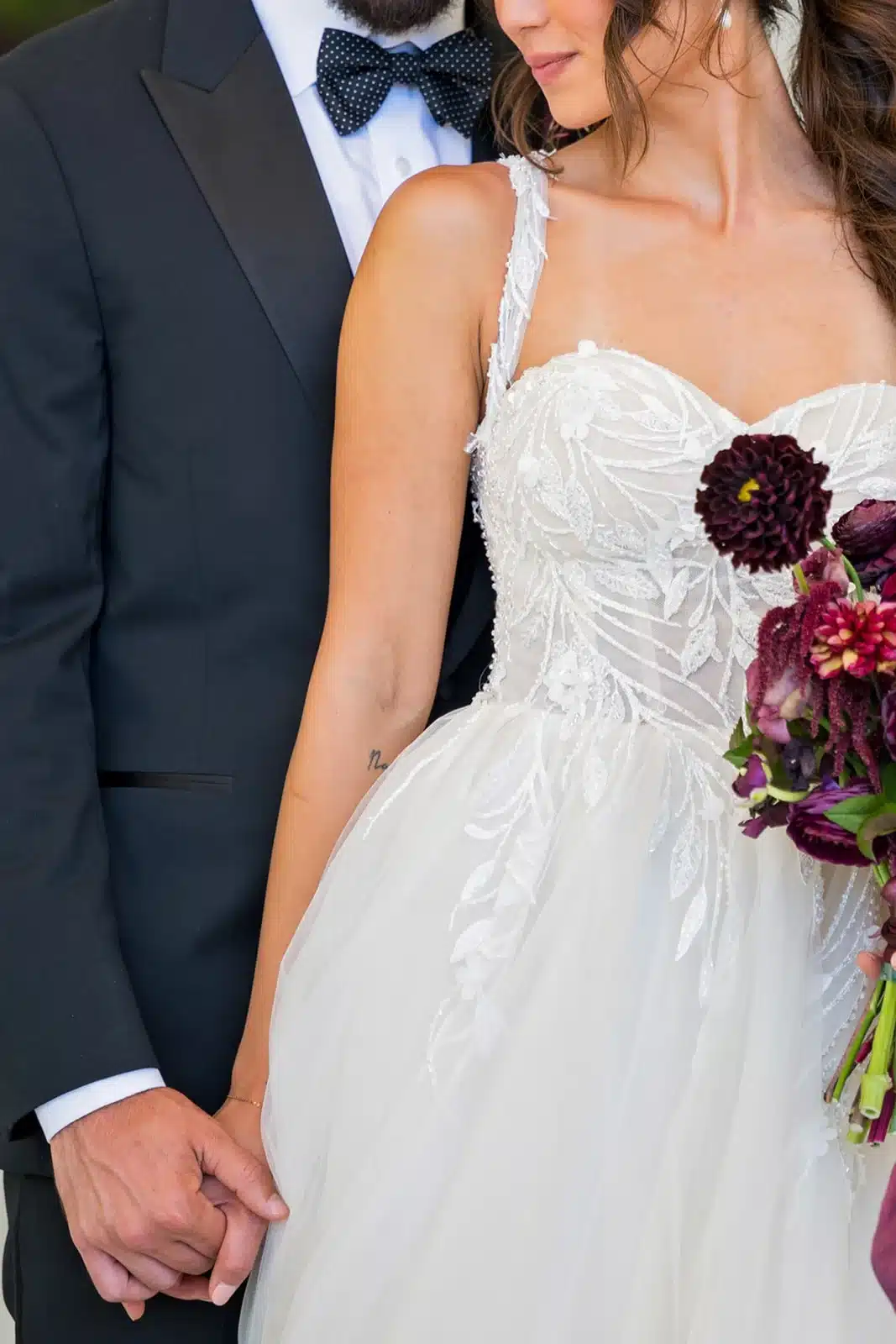 Bride in white dress with burgundy bouquet and groom in navy suit.
