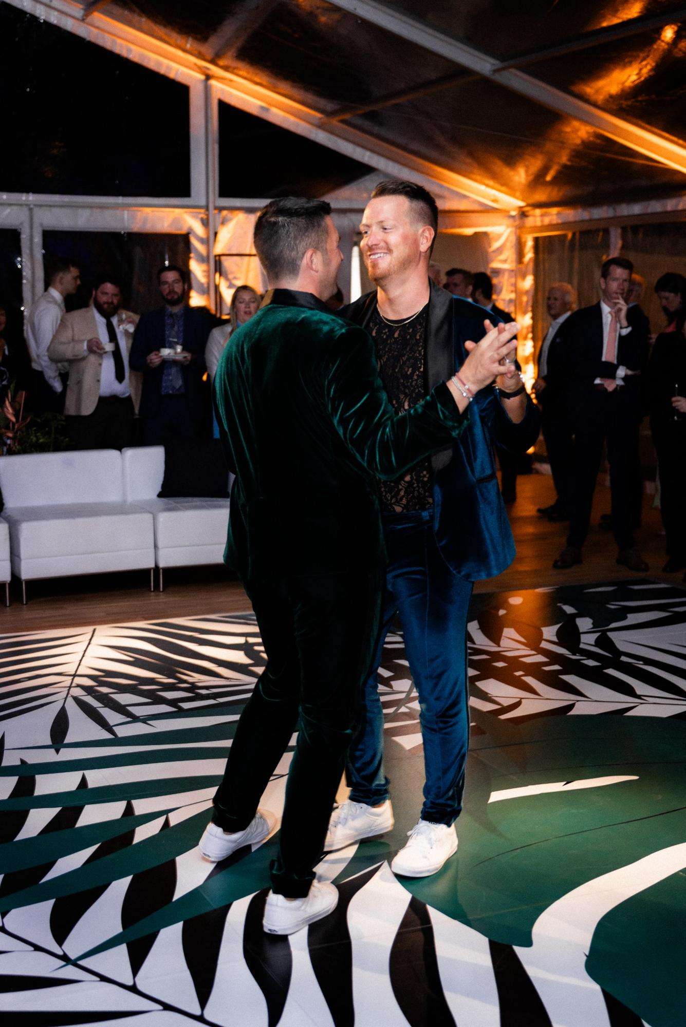 Grooms dancing together in matching velvet jackets on custom dance floor. Grooms dancing together in matching velvet jackets on custom dance floor.