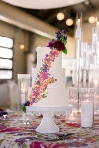FOXTOWN STYLED SHOOT-251 Three-tier wedding cake with brightly colored cascading flower accents on white cake stand