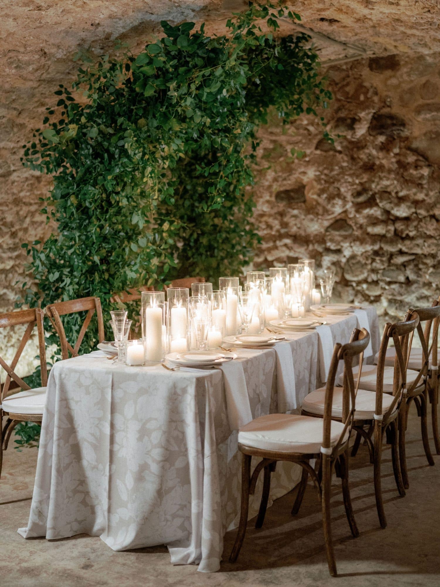 Long table with candles filled across the top, light colored linens and natural colored chairs. Long table with candles filled across the top, light colored linens and natural colored chairs.