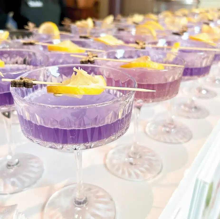 Neat Beverage Catering, Purple Signature Cocktail with Lemon Garnish Neat Beverage Catering, Purple Signature Cocktail with Lemon Garnish
